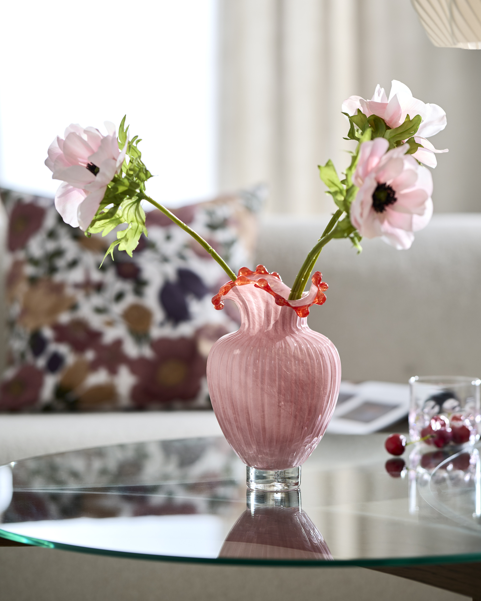 En rosa vas med konstblommor står på ett soffbord med glasskiva