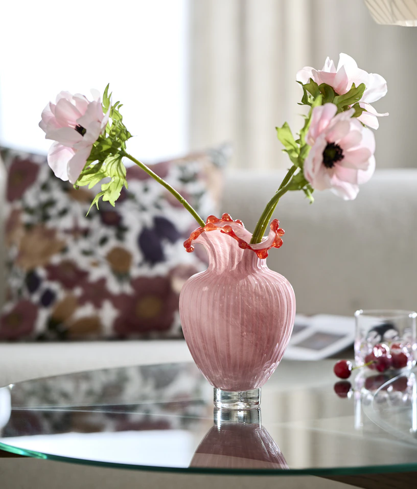 En rosa vas med konstblommor står på ett soffbord med glasskiva