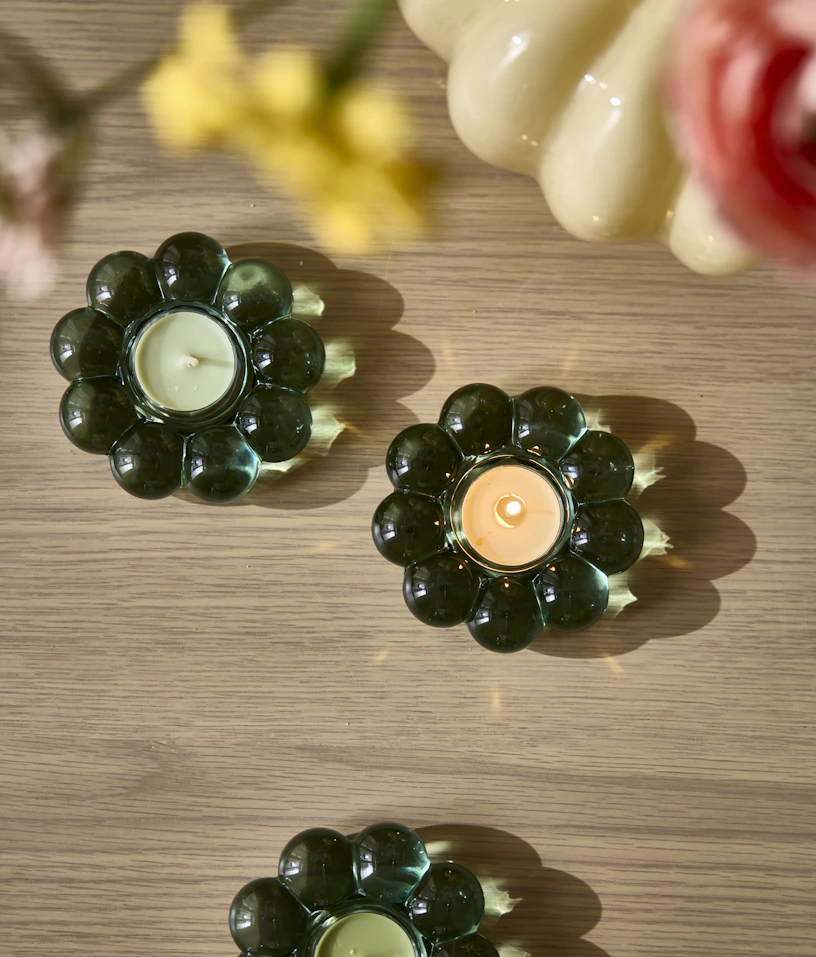 tre små gröna ljushållare i form av en blomma står på ett ljust träbord