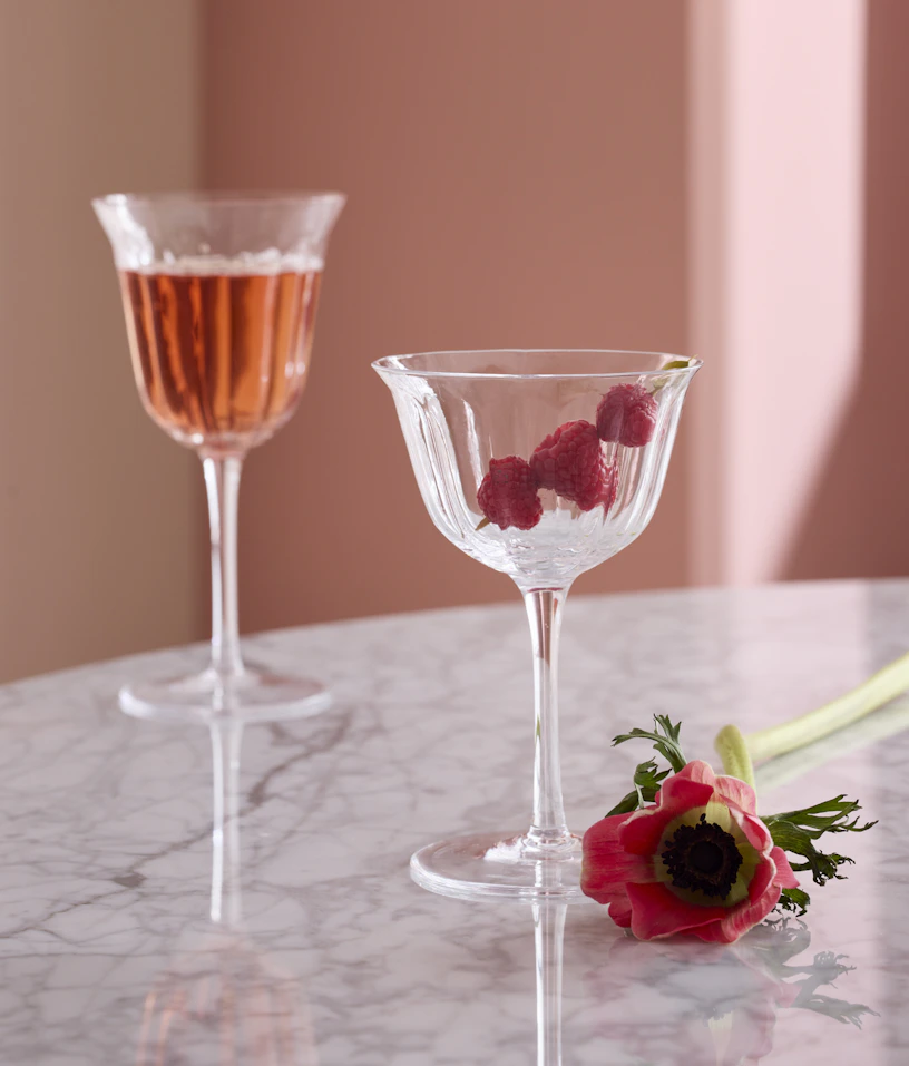 Två vinglas står på ett marmorbord med hallon och rosa dryck i