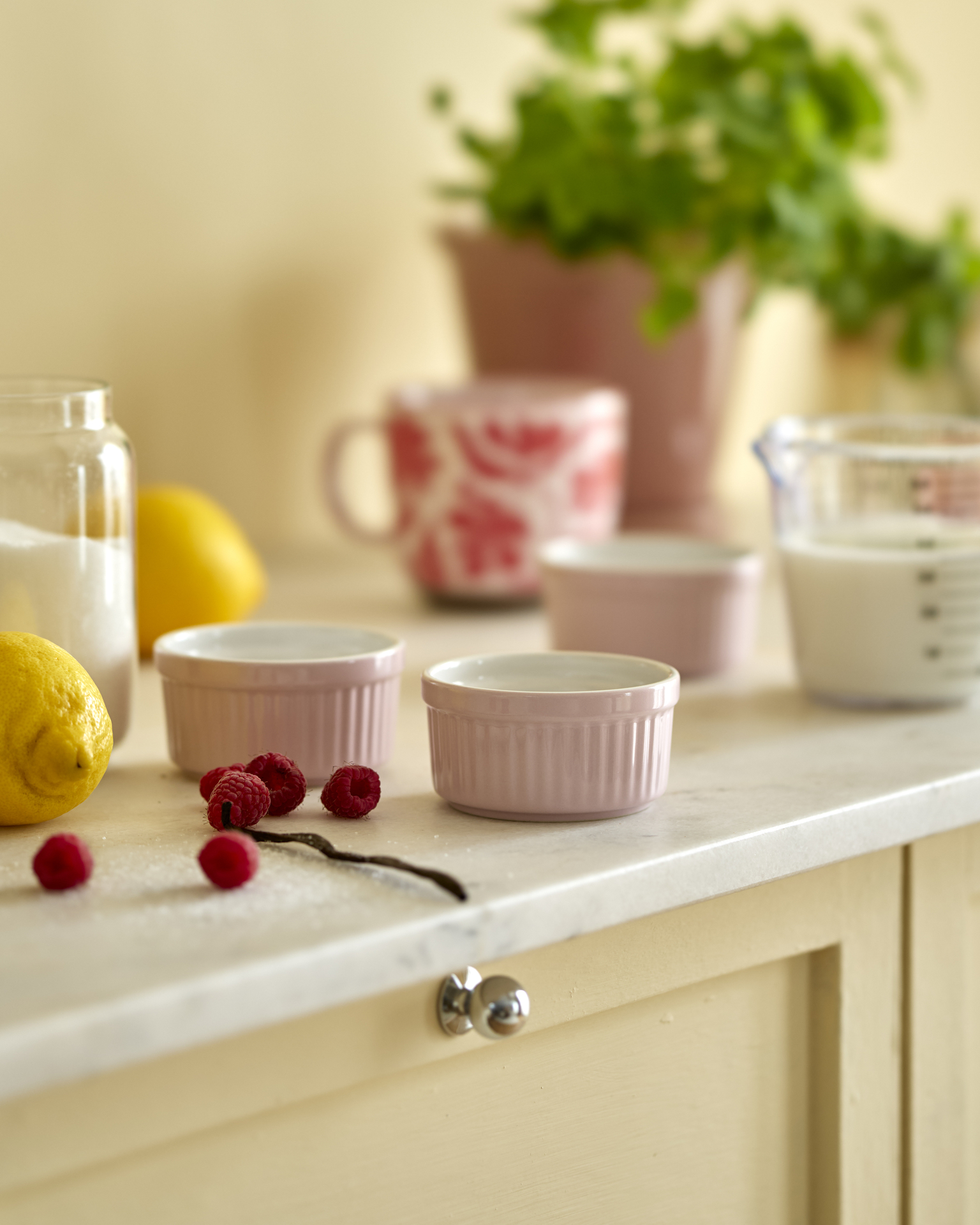 Rosa små bakformar står på en köksbänk tillsammans med hallon och citroner