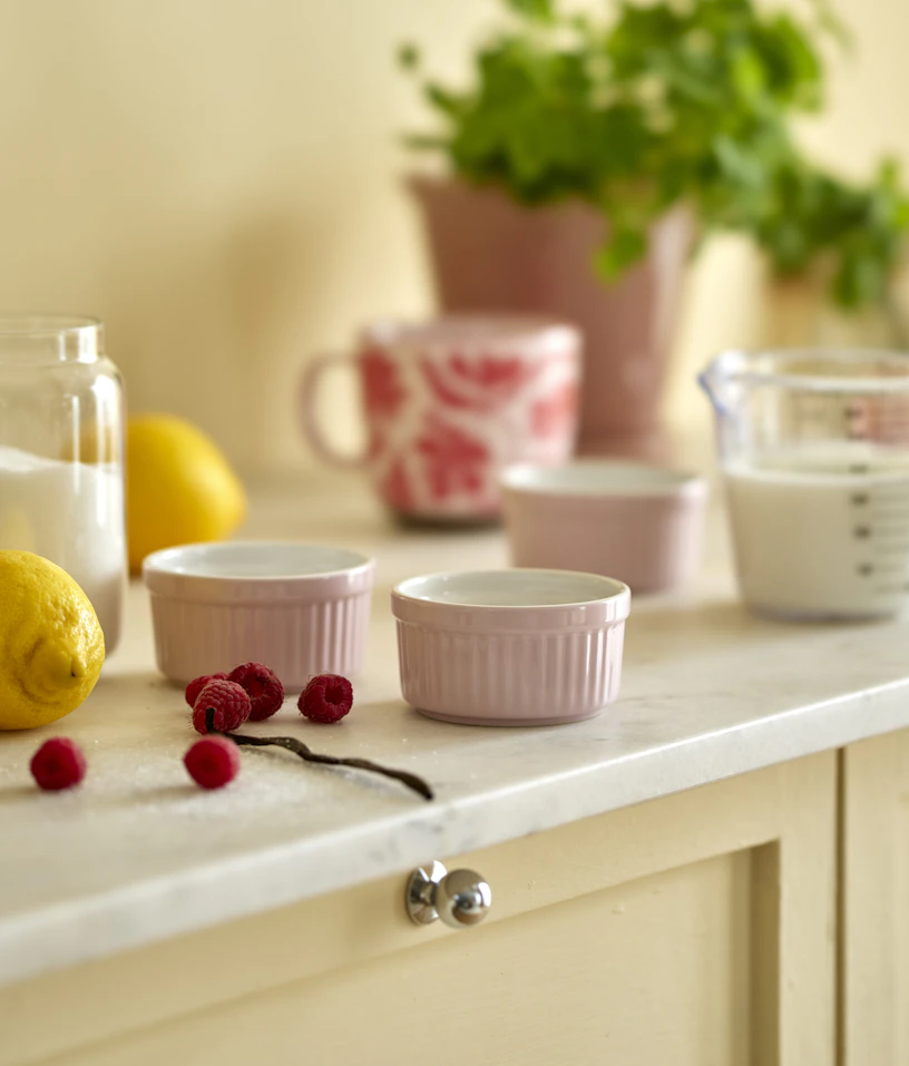 Rosa små bakformar står på en köksbänk tillsammans med hallon och citroner