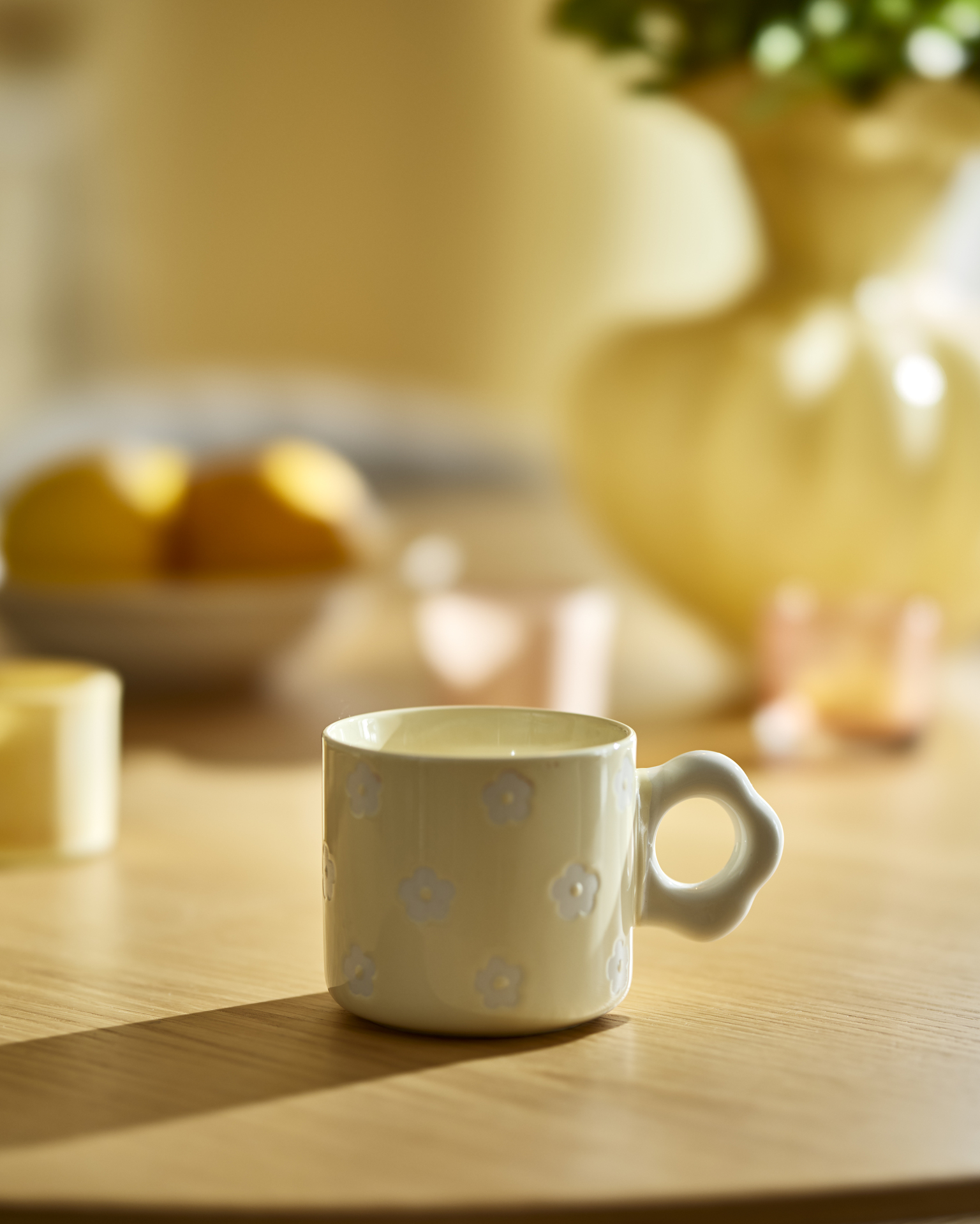 En gul kaffekopp med vita blommor står på ett ljust träbord