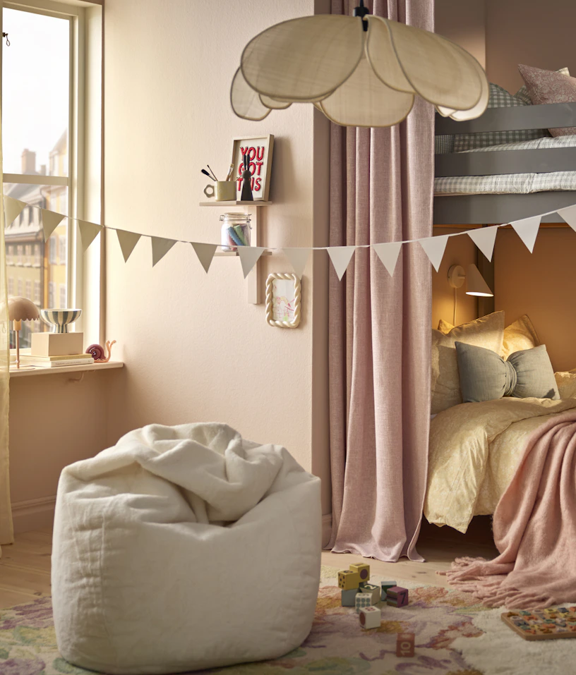 En beige sittsäck står i ett barnrum med rosa väggar och en vimpel hängandes genom rummet