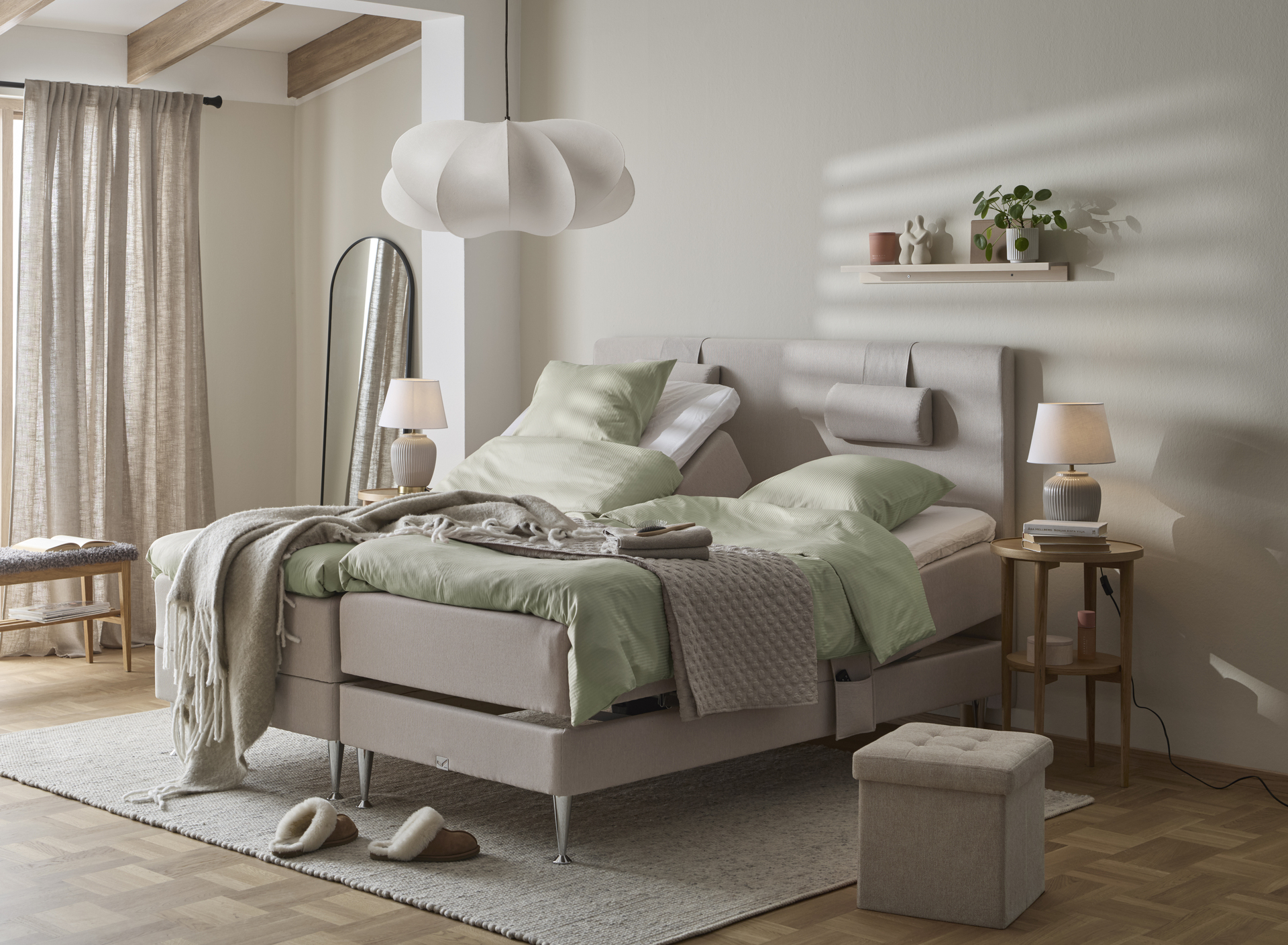 Sovrum med grå väggar och en stor grå ställbar kontinentalsäng i mitten på rummet med ljusgröna sängkläder. 