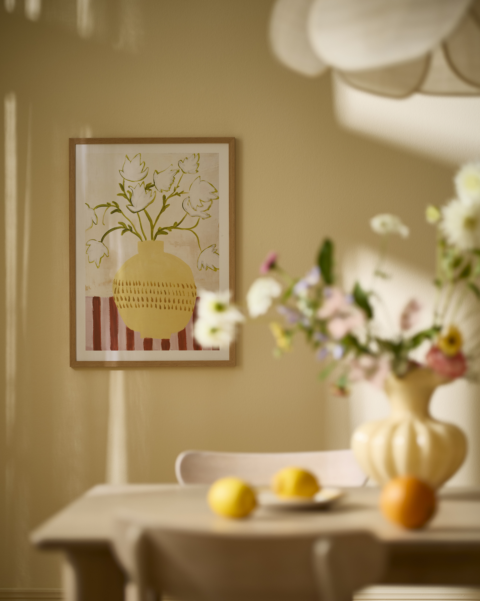 en tavlka med motiv av en vas med blommor hänger på en gul vägg