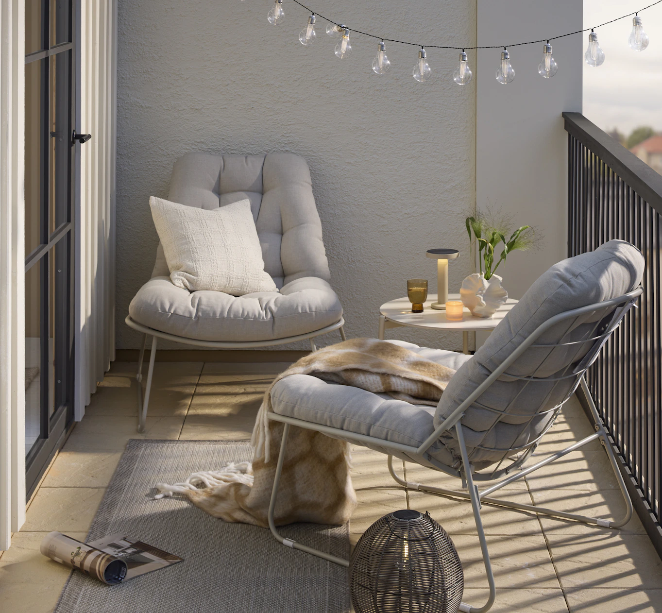 En balkong är möblerad med två beiga fåtöljer, ett runt bord med en portabel lampa och en ljusslinga.