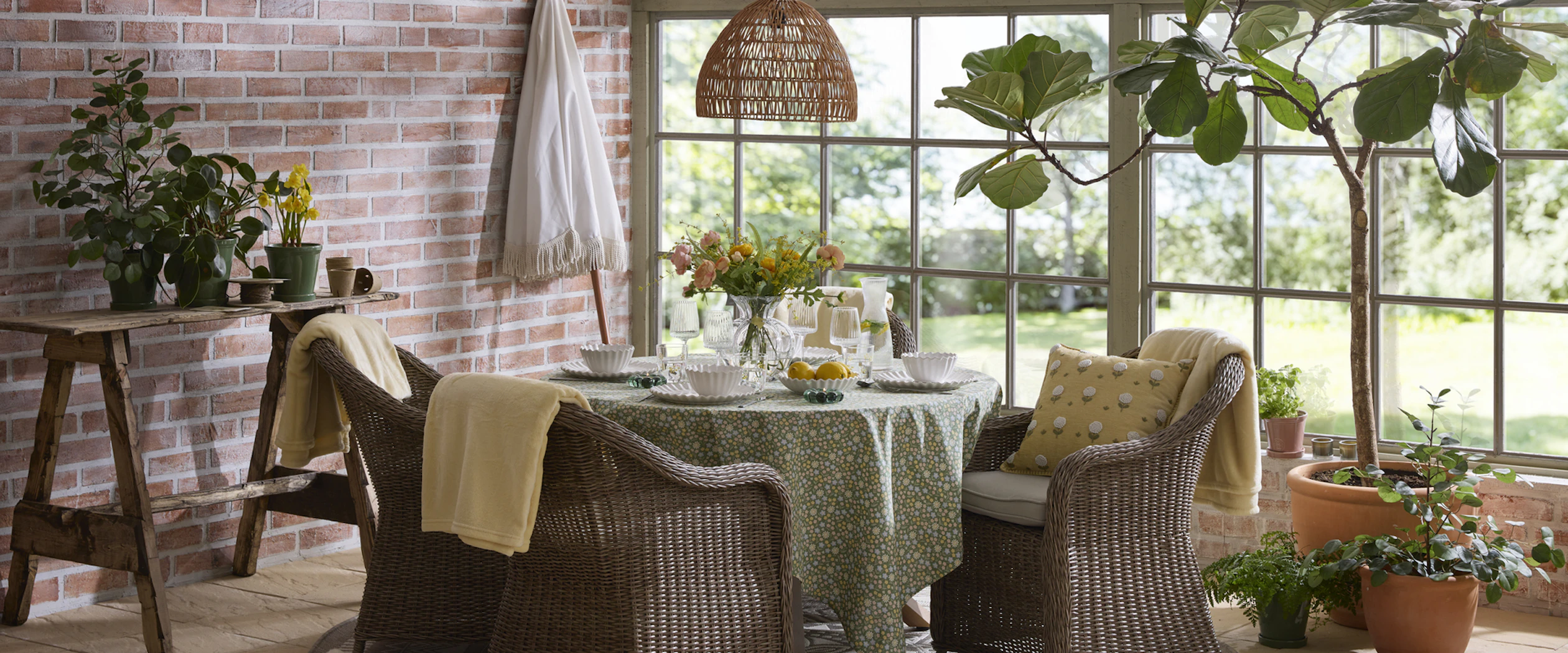 En utesoffgrupp med runt bord och fyra fåtöljer i konstrotting står i ett orangeri fyllt av växter.