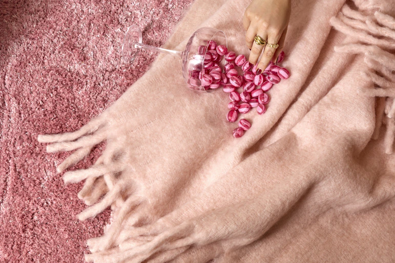 På en rosa pläd ligger en vält skål med rosa godis, som en hand sträcker sig efter.