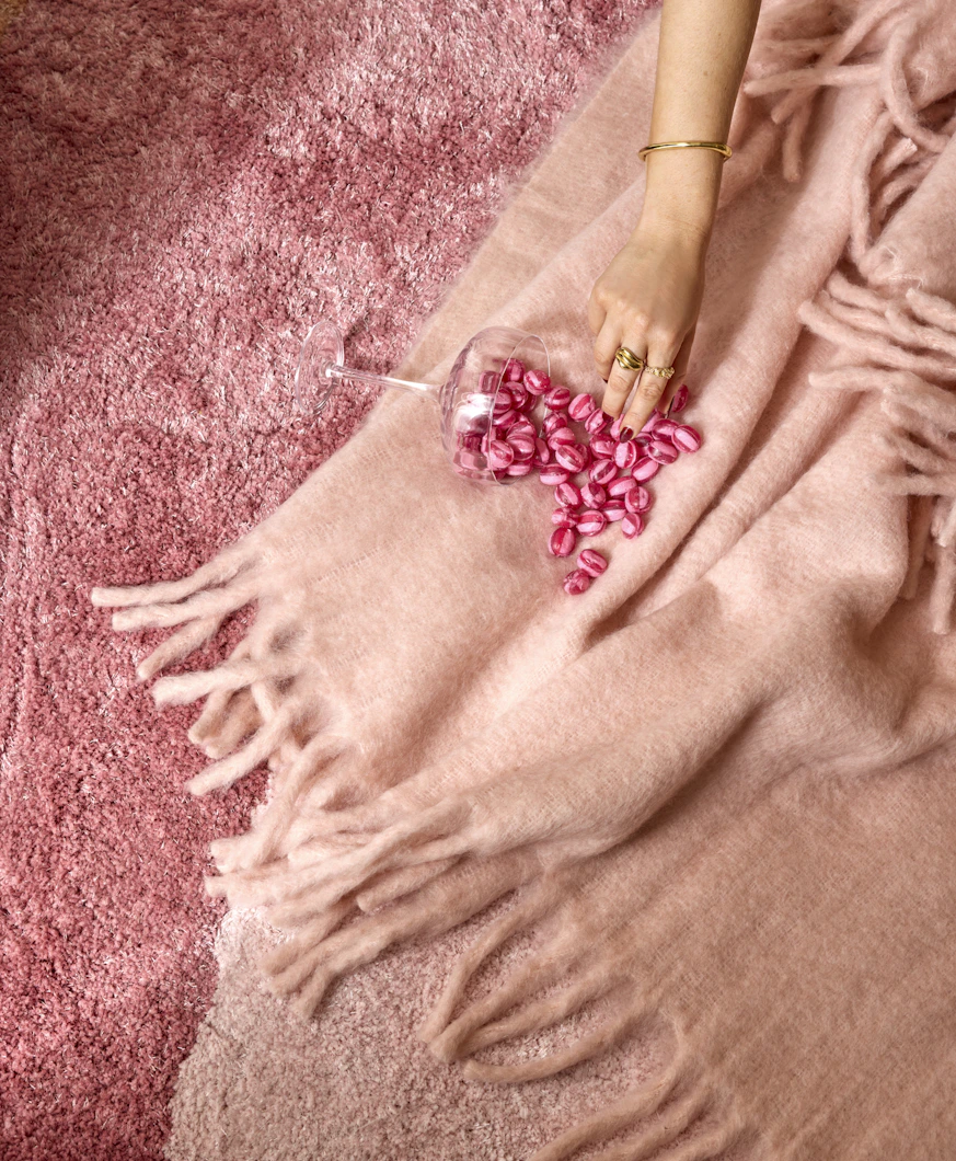 På en rosa pläd ligger en vält skål med rosa godis, som en hand sträcker sig efter.