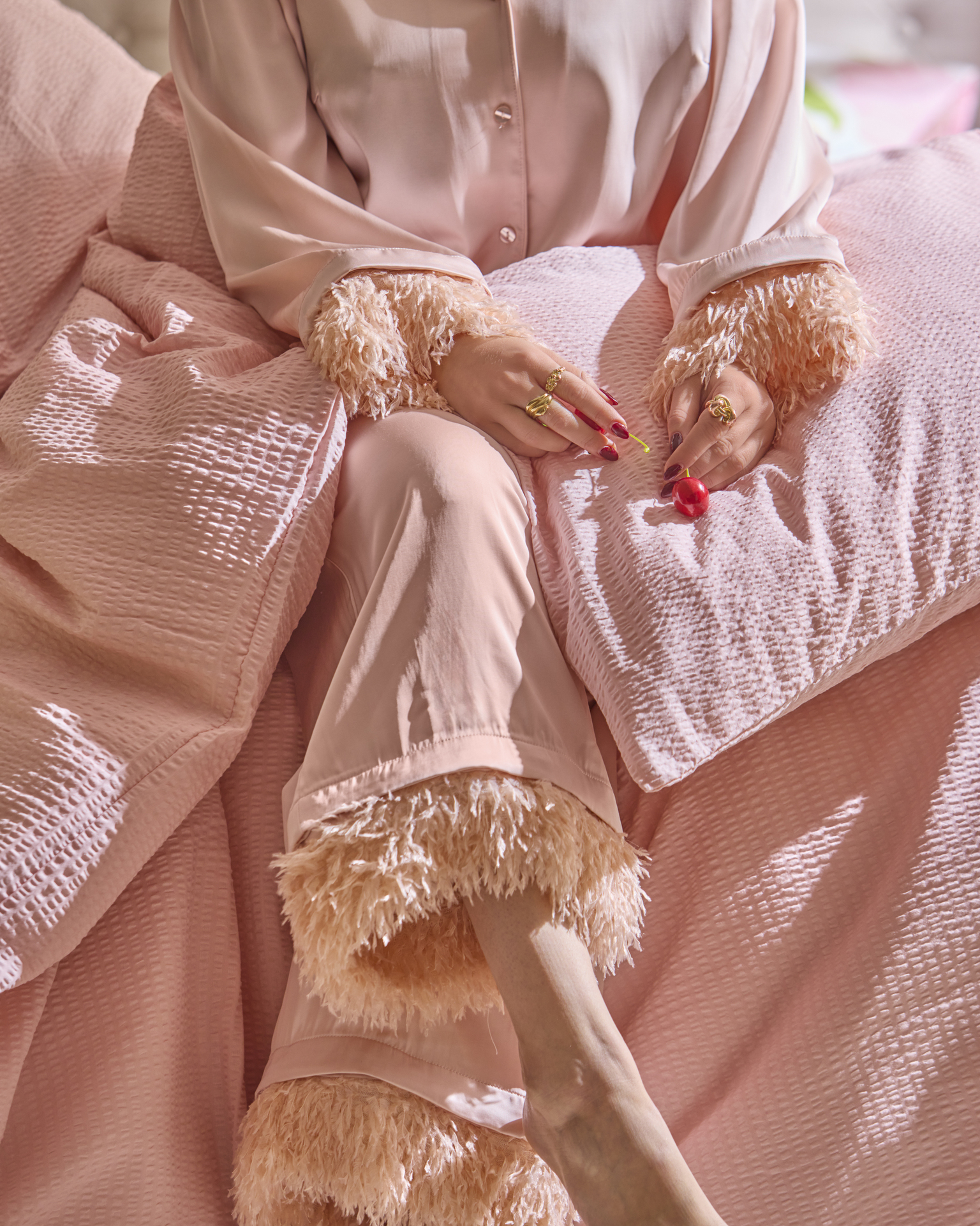 Kvinna i rosa pyjamas sitter bland sängkläder i matchande färg.