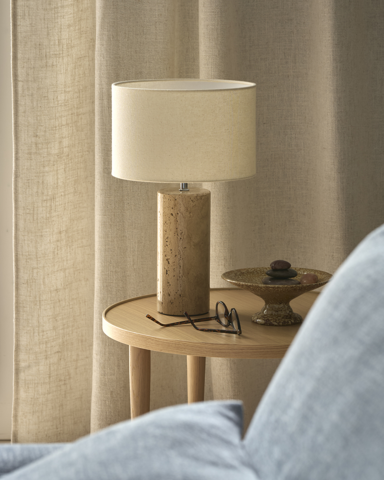 På ett sidobord i ek står en bordslampa i sandsten med vit lampskärm