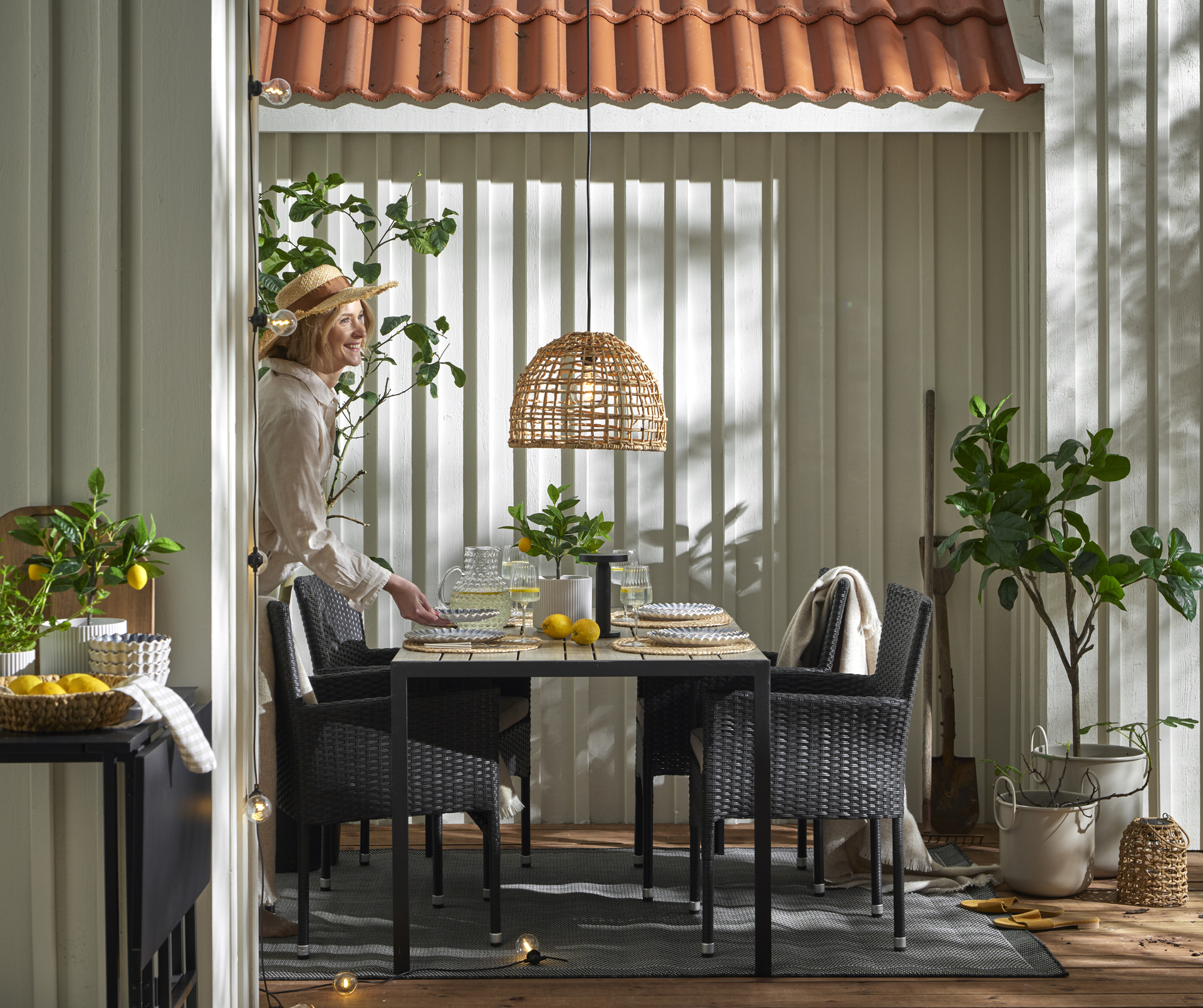 En kvinna dukar ett mörkt utebord i konstträ med fyra matchande utefåtöljer i konstrotting.