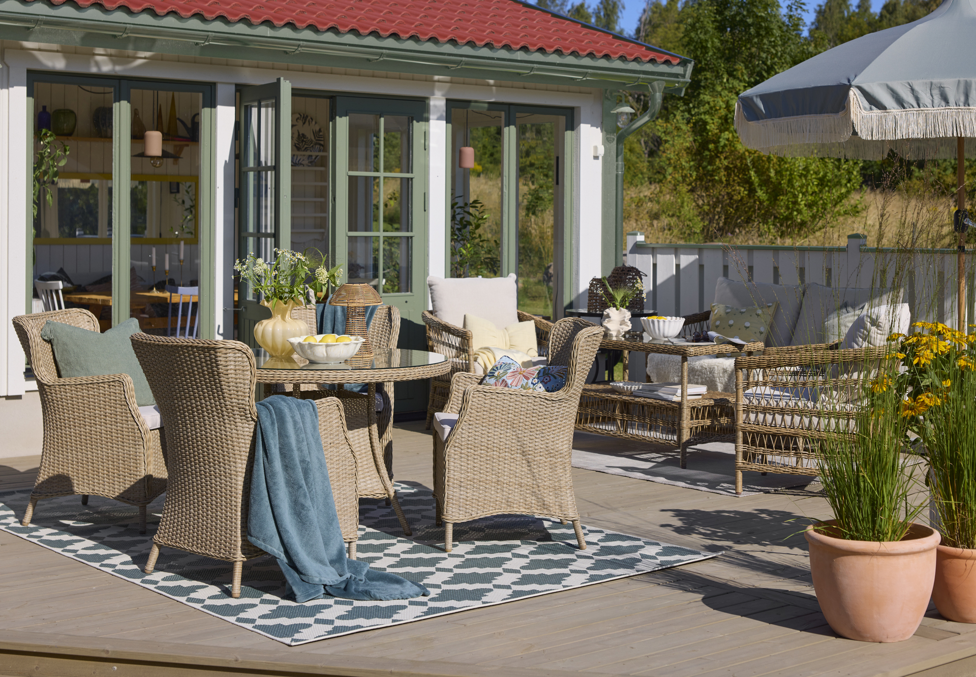 Ett runt utebord i konstrotting och glasskiva med fyra matchande fåtöljer står på en blåmönstrad utematta.