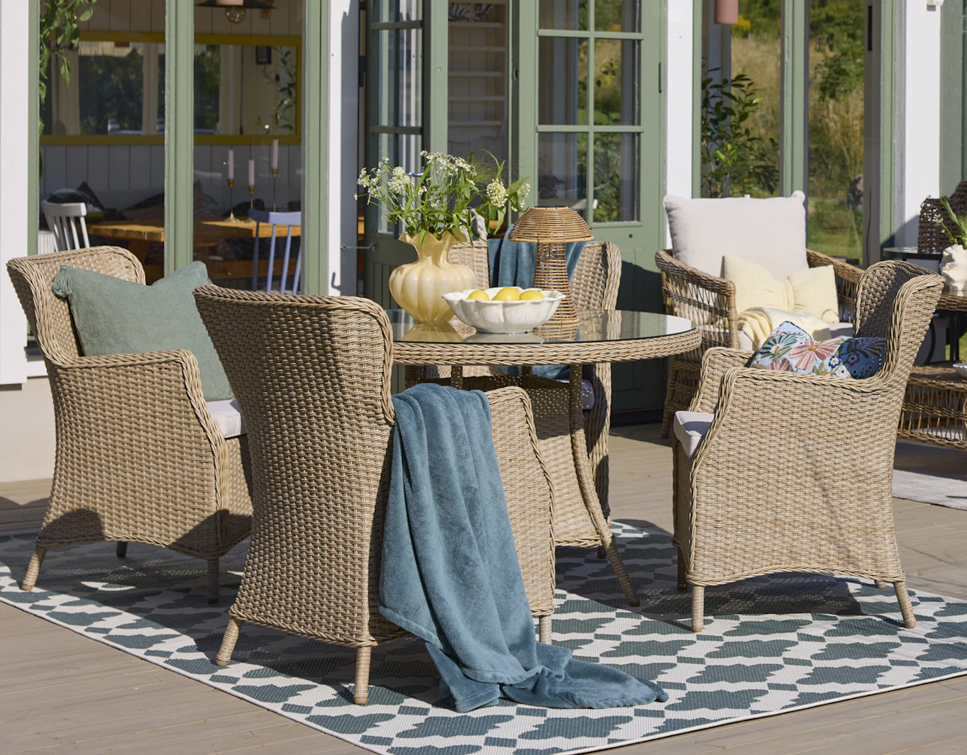 Ett runt utebord i konstrotting och glasskiva med fyra matchande fåtöljer står på en blåmönstrad utematta.