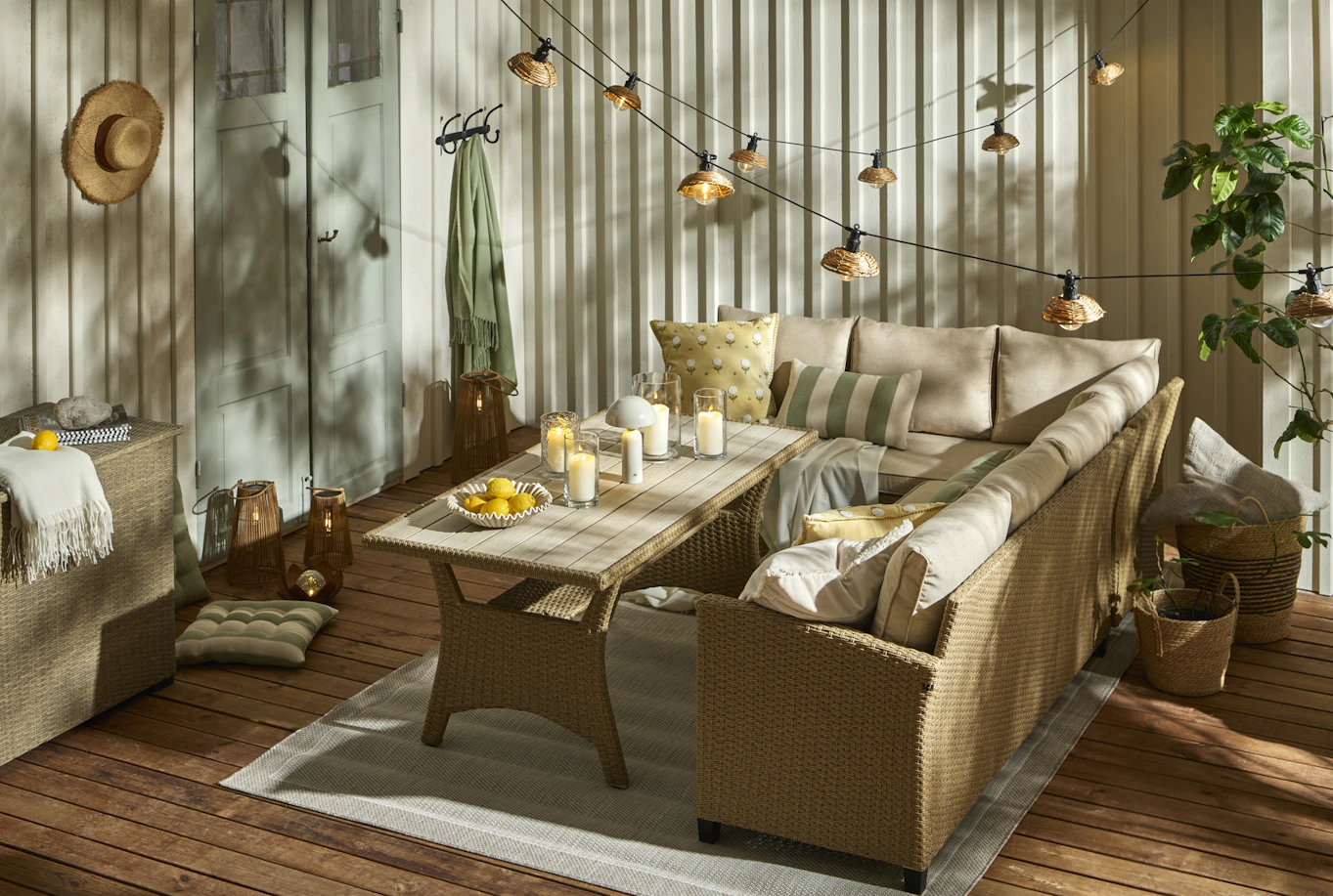 En hörnsoffa i konstrotting är dekorerad med gula och gröna kuddar. Framför soffan står ett matchande soffbord och över soffan hänger en ljusslinga.