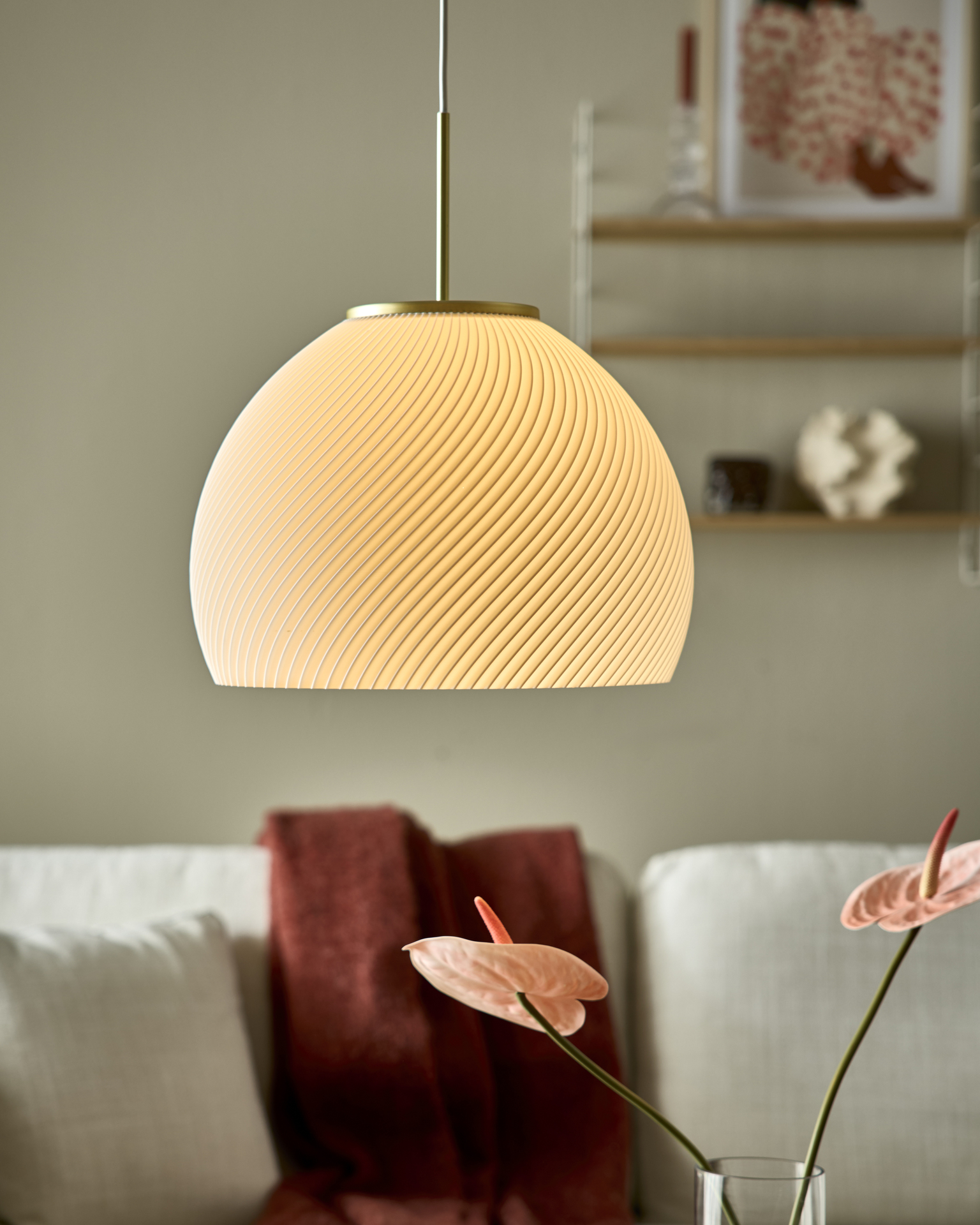 3D-printad vit taklampa med mässingsdetaljer hänger framför en soffa med en röd filt.