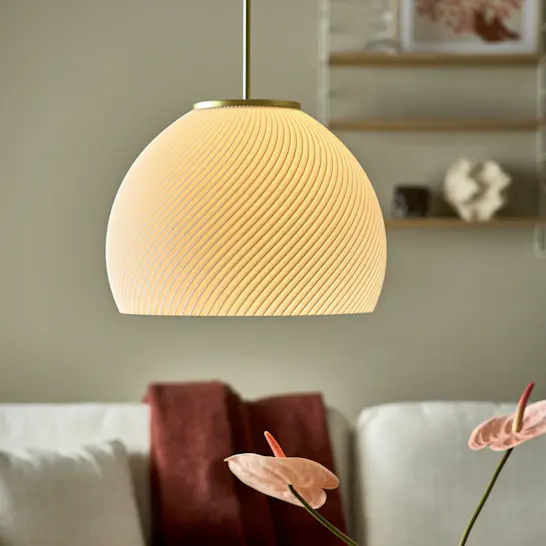 3D-printad vit taklampa med mässingsdetaljer hänger framför en soffa med en röd filt.