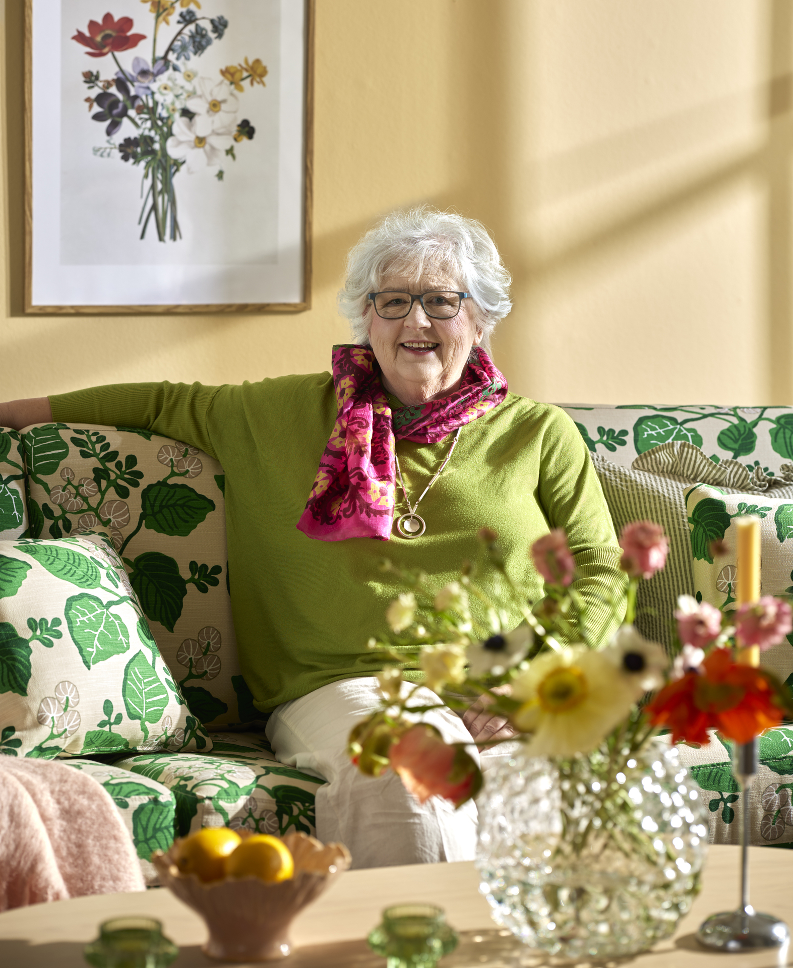 I en soffa klädd i det mönstrade tyget "Sommardag"sitter Birgitta Johnsson-Nyysti, designern bakom tyget