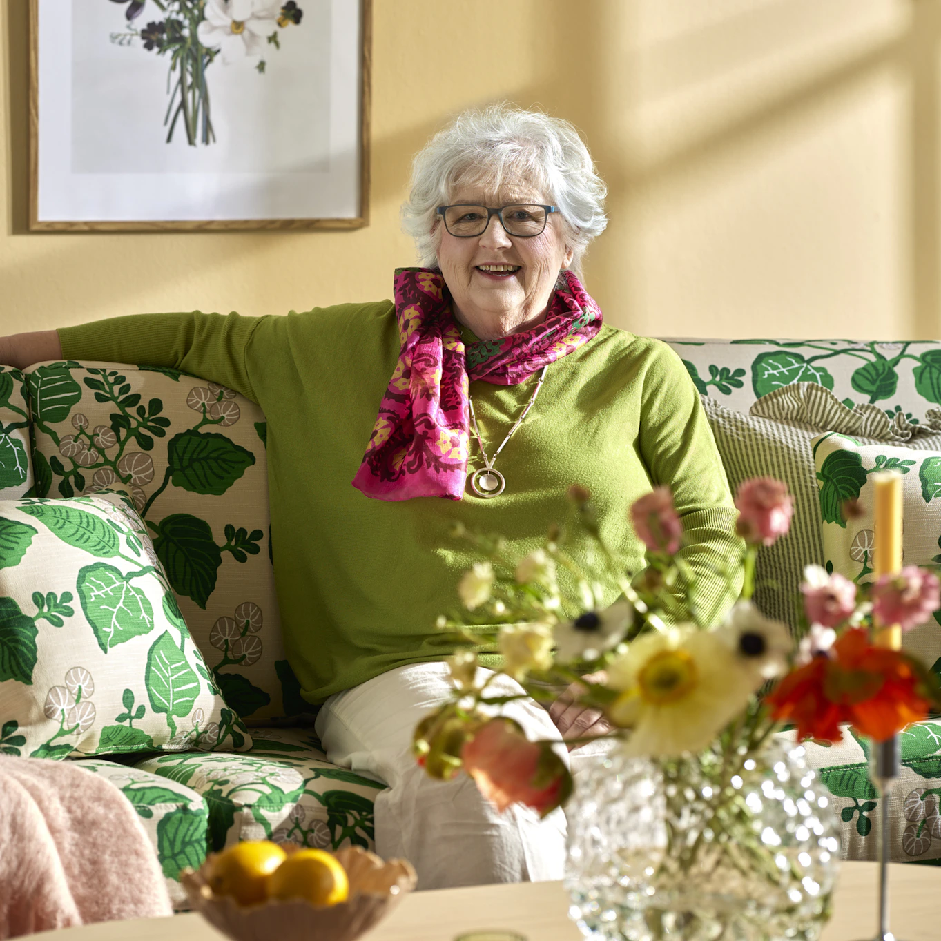 I en soffa klädd i det mönstrade tyget "Sommardag"sitter Birgitta Johnsson-Nyysti, designern bakom tyget