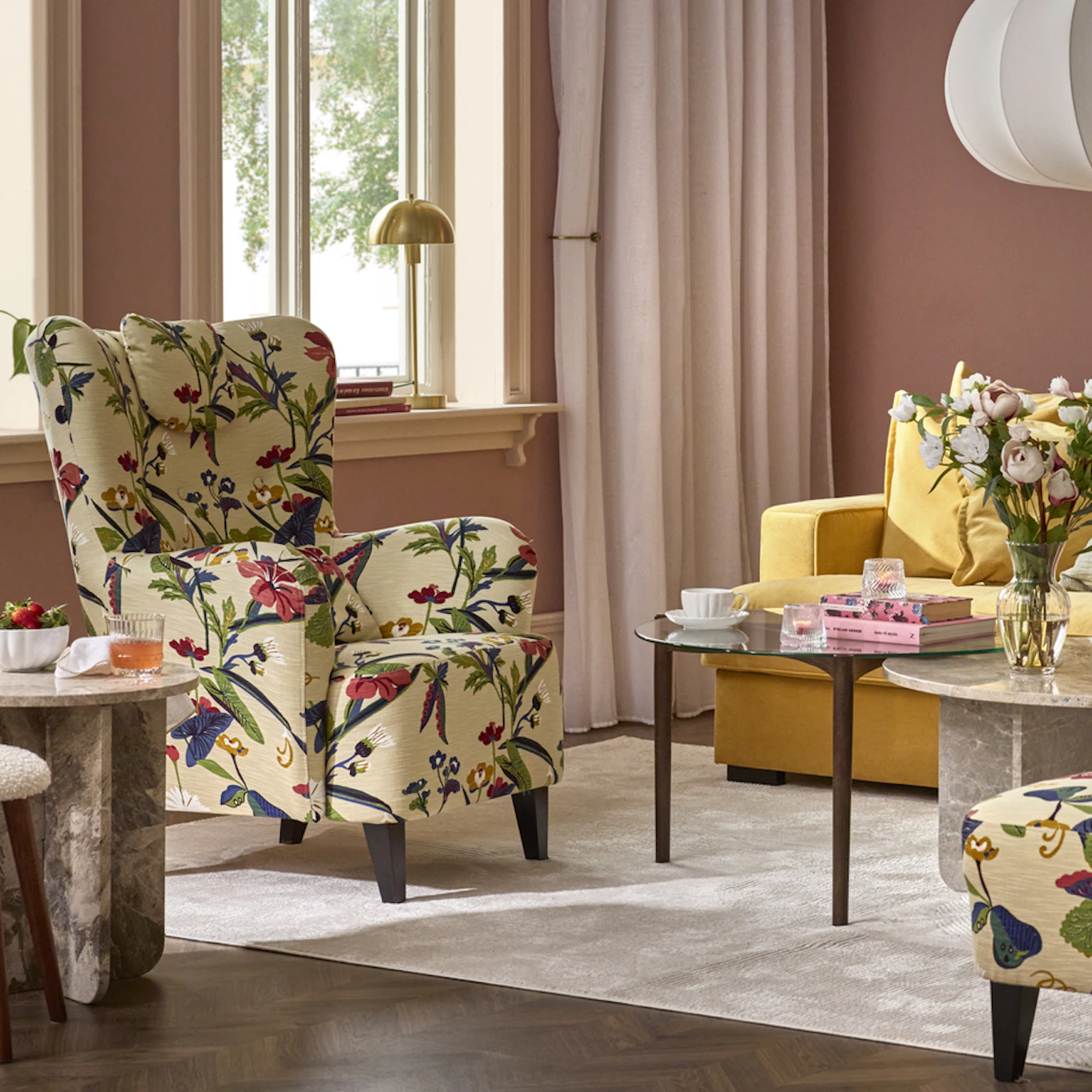 I ett rosa vardagsrum står en fåtölj i blommigt mönster intill ett sidobord i marmor.