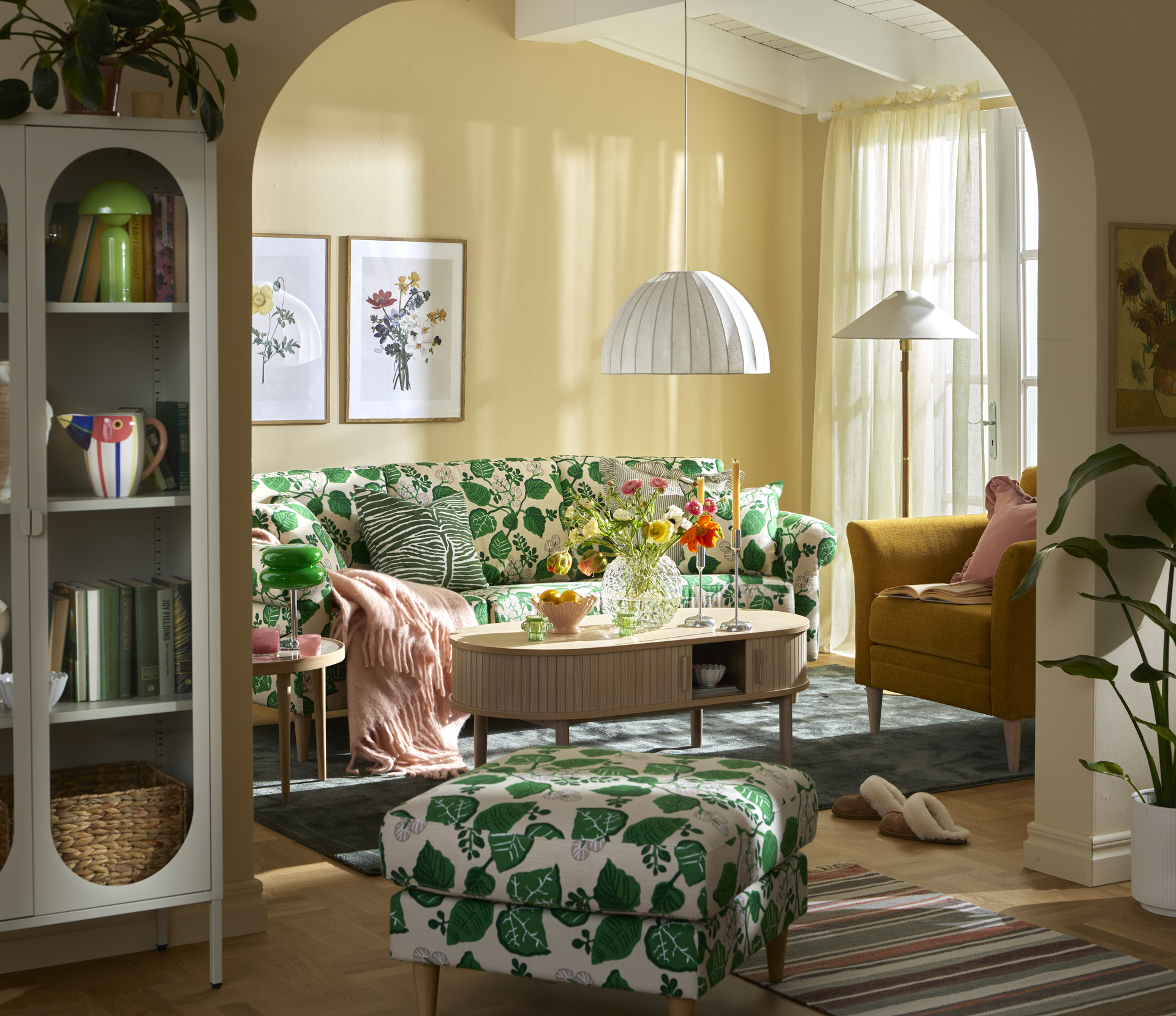 En grönmönstrad soffa står bakom ett soffbord i ek i ett vardagsrum målat i gult.