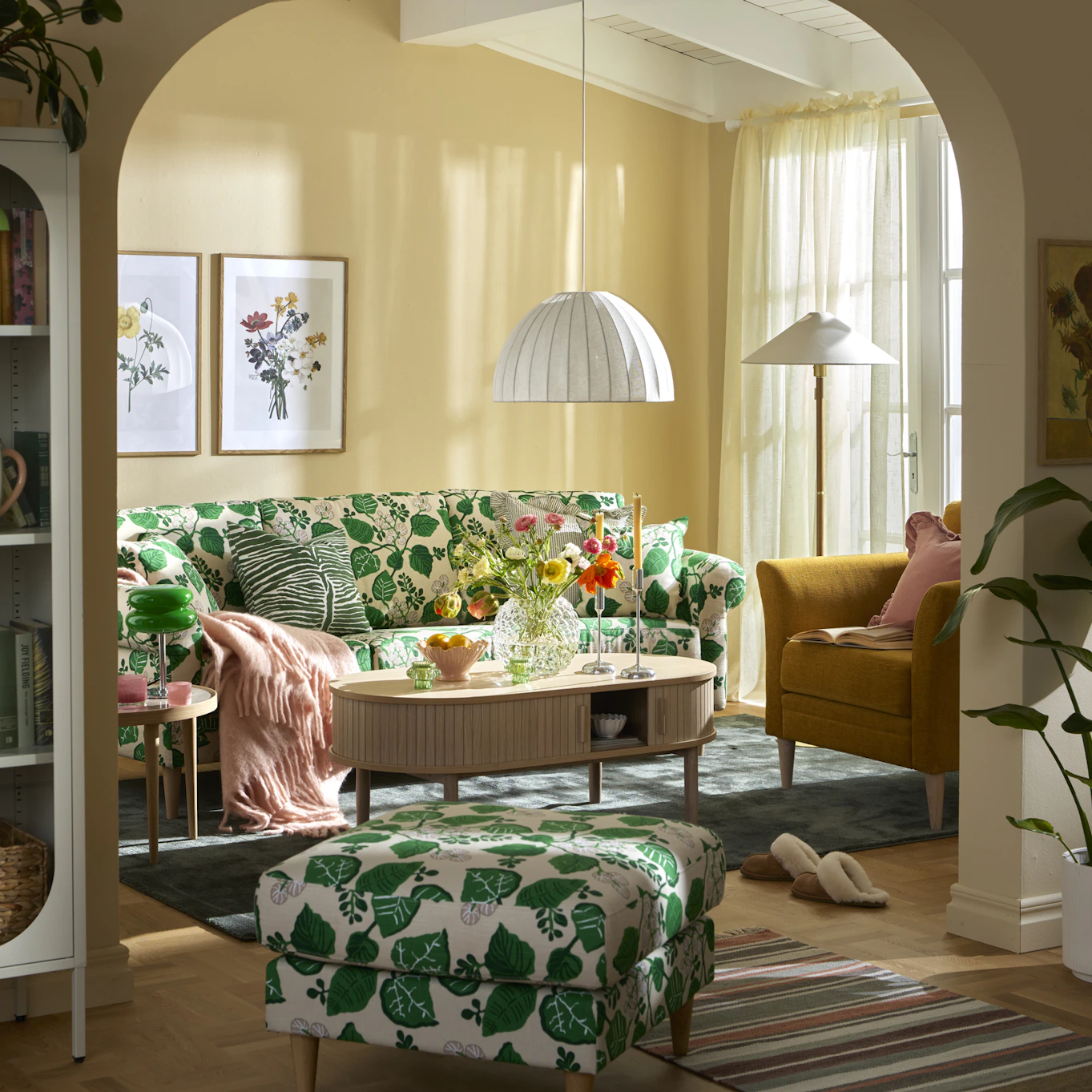 En grönmönstrad soffa står bakom ett soffbord i ek i ett vardagsrum målat i gult.