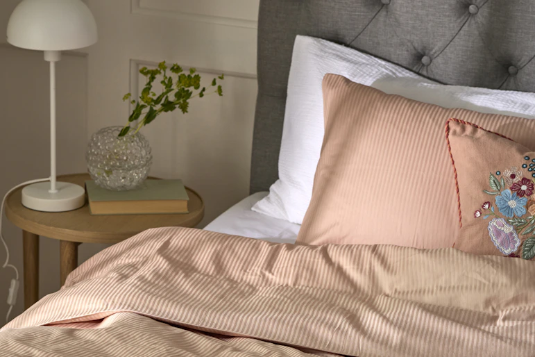 En säng med grå sänggavel är bäddad med randiga sängkläder i rosa.