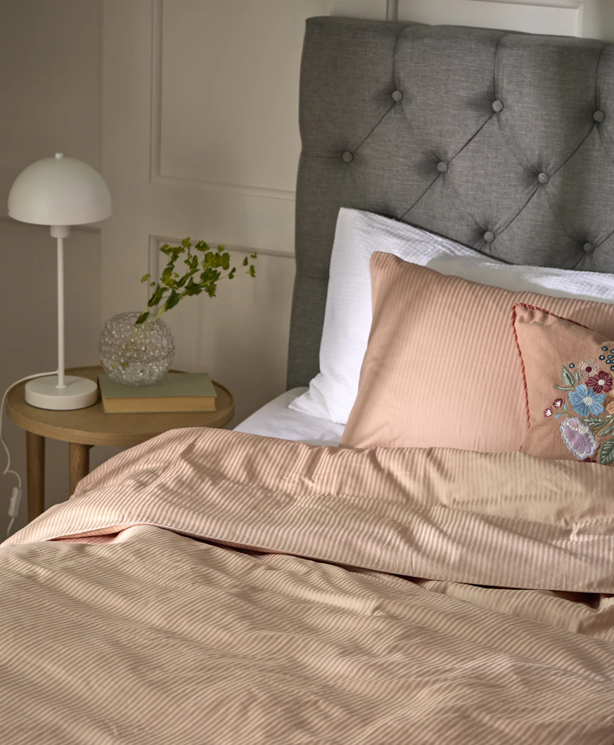 En säng med grå sänggavel är bäddad med randiga sängkläder i rosa.