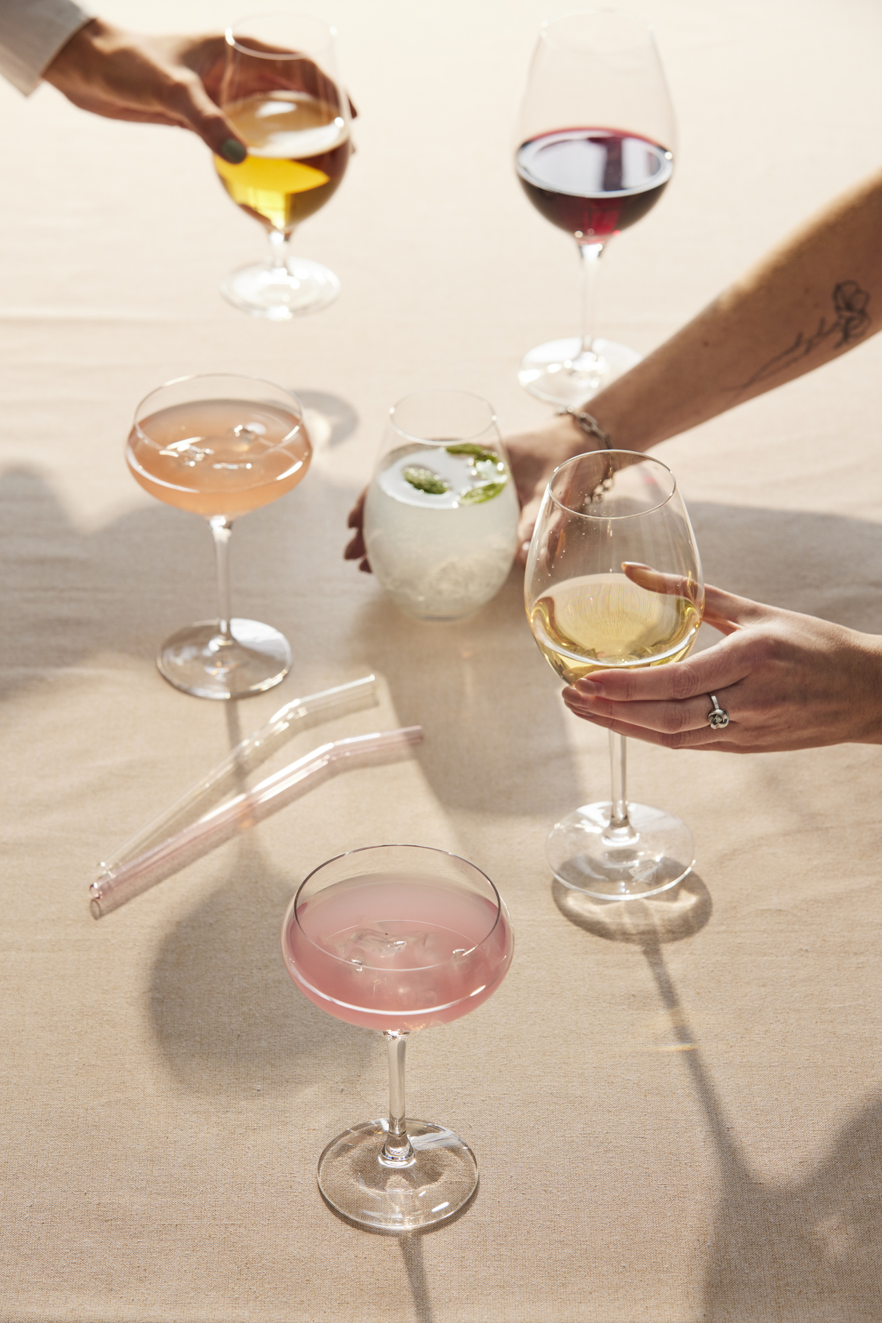 Flera händer stäcker sig över ett bord och skålar i glas fyllda med olika sorters drinkar.