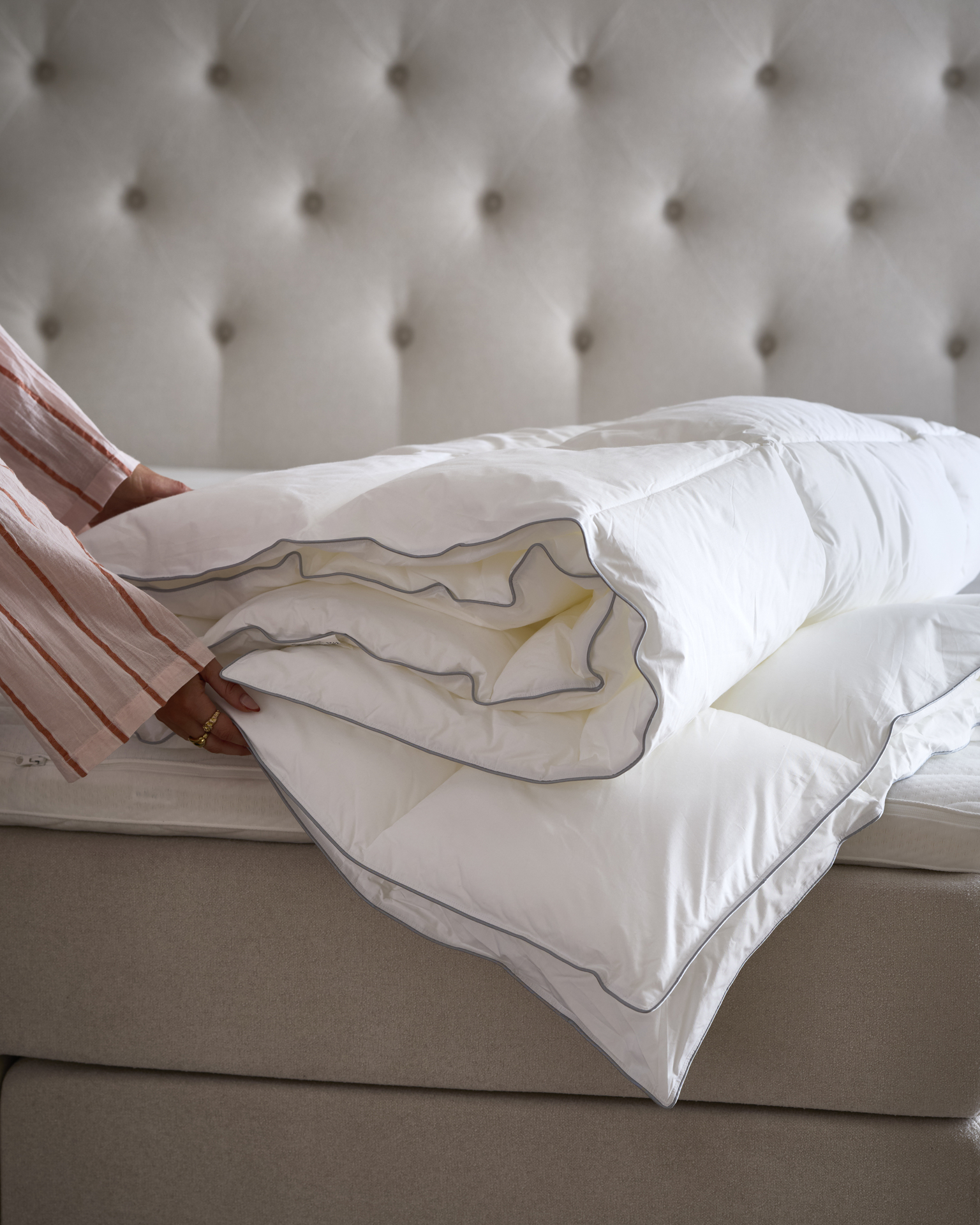 Händer håller i ett vikt täcke som ligger på en obäddad säng.