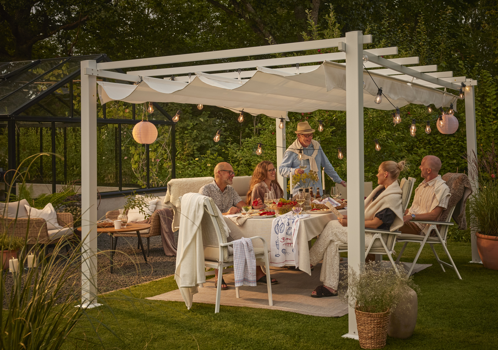 Ett sällskap njuter av kräftskiva i en trädgård under en pergola full av ljusslingor.