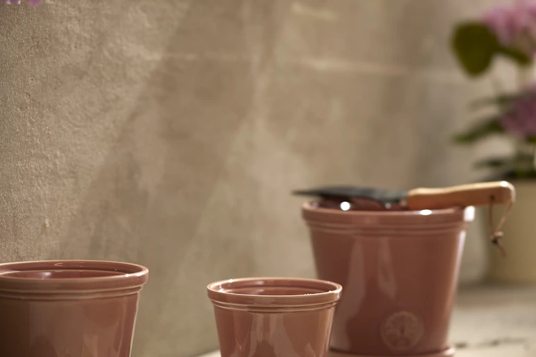 Tre rosa krukor i olika storlekar står framför en beige stenvägg.