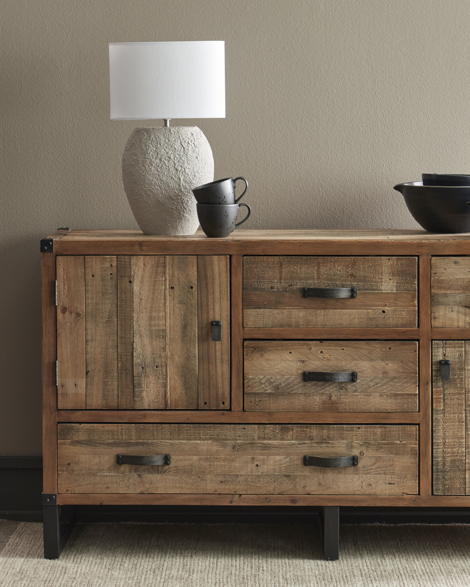 En lampa och svart porslin står på en skänk i rustikt trä.