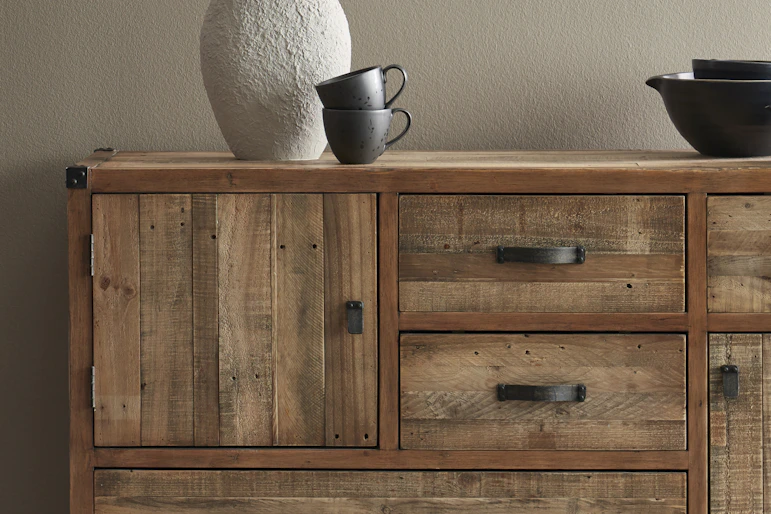 En lampa och svart porslin står på en skänk i rustikt trä.