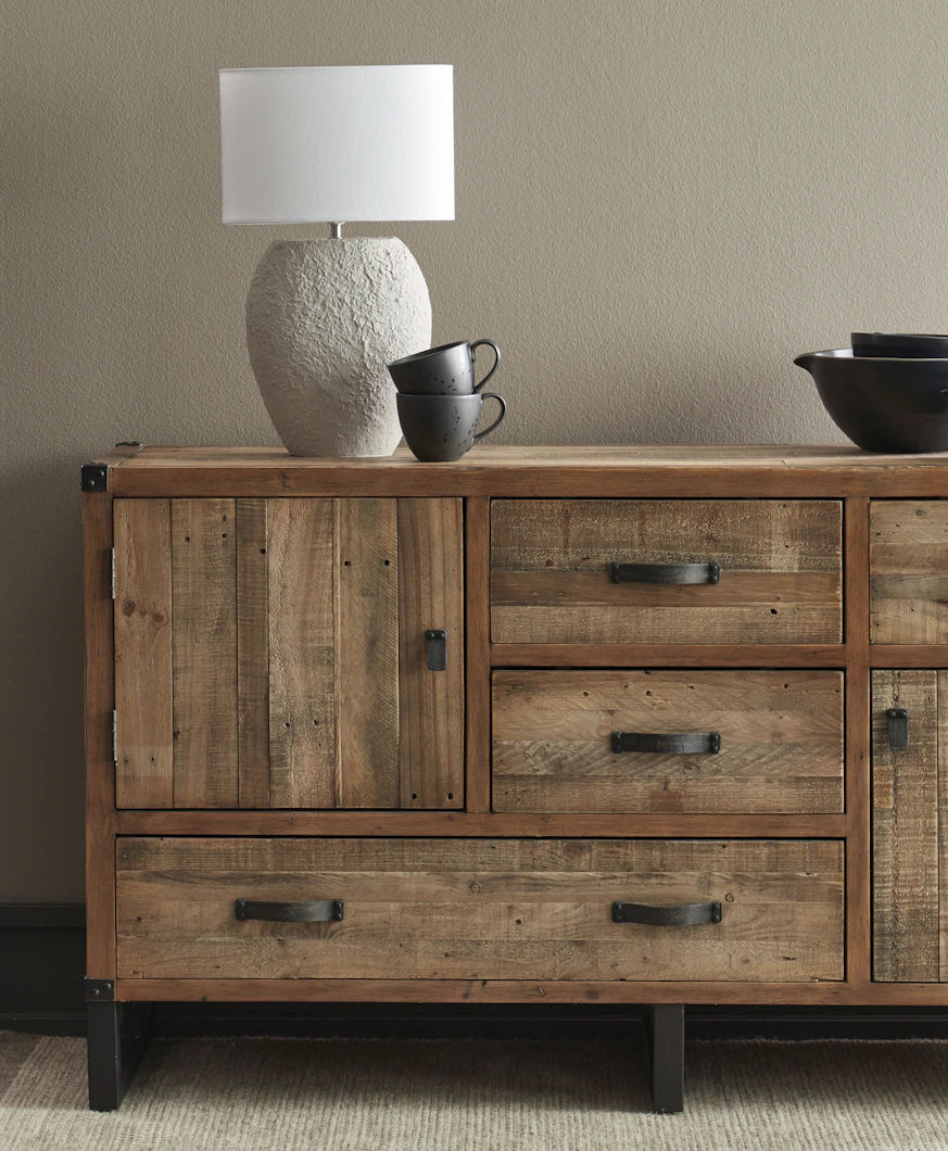 En lampa och svart porslin står på en skänk i rustikt trä.