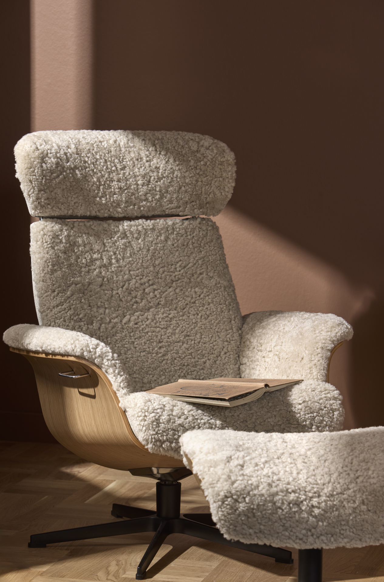 En fåtölj klädd i vitt fårskinn står framför en terrakottafärgad vägg.