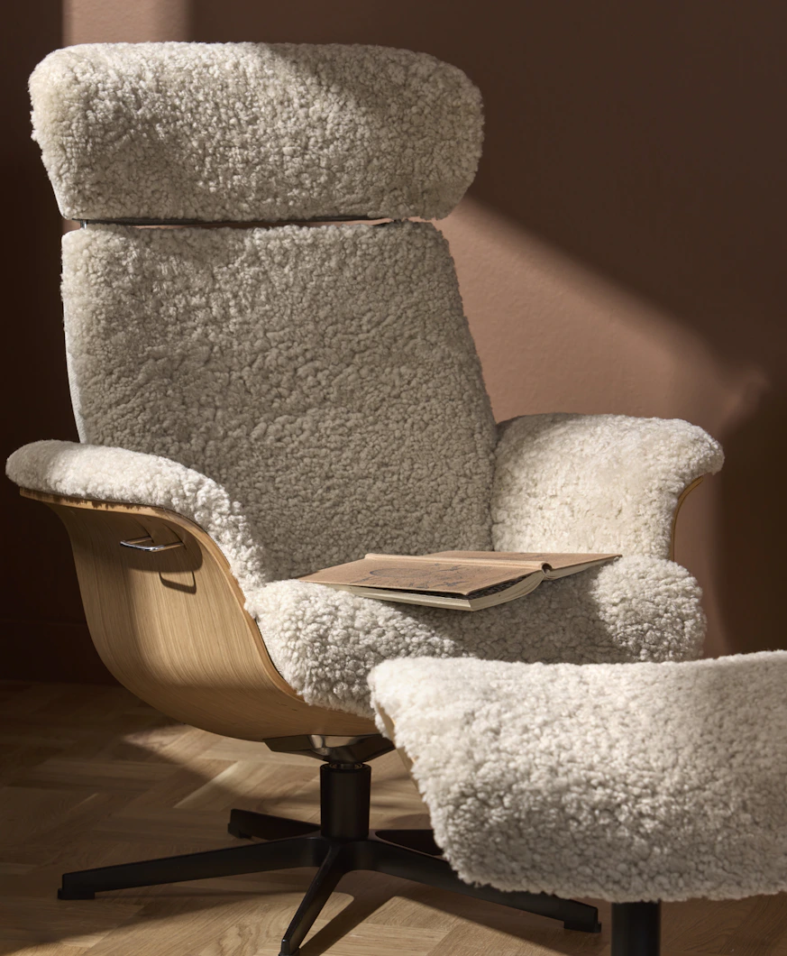 En fåtölj klädd i vitt fårskinn står framför en terrakottafärgad vägg.