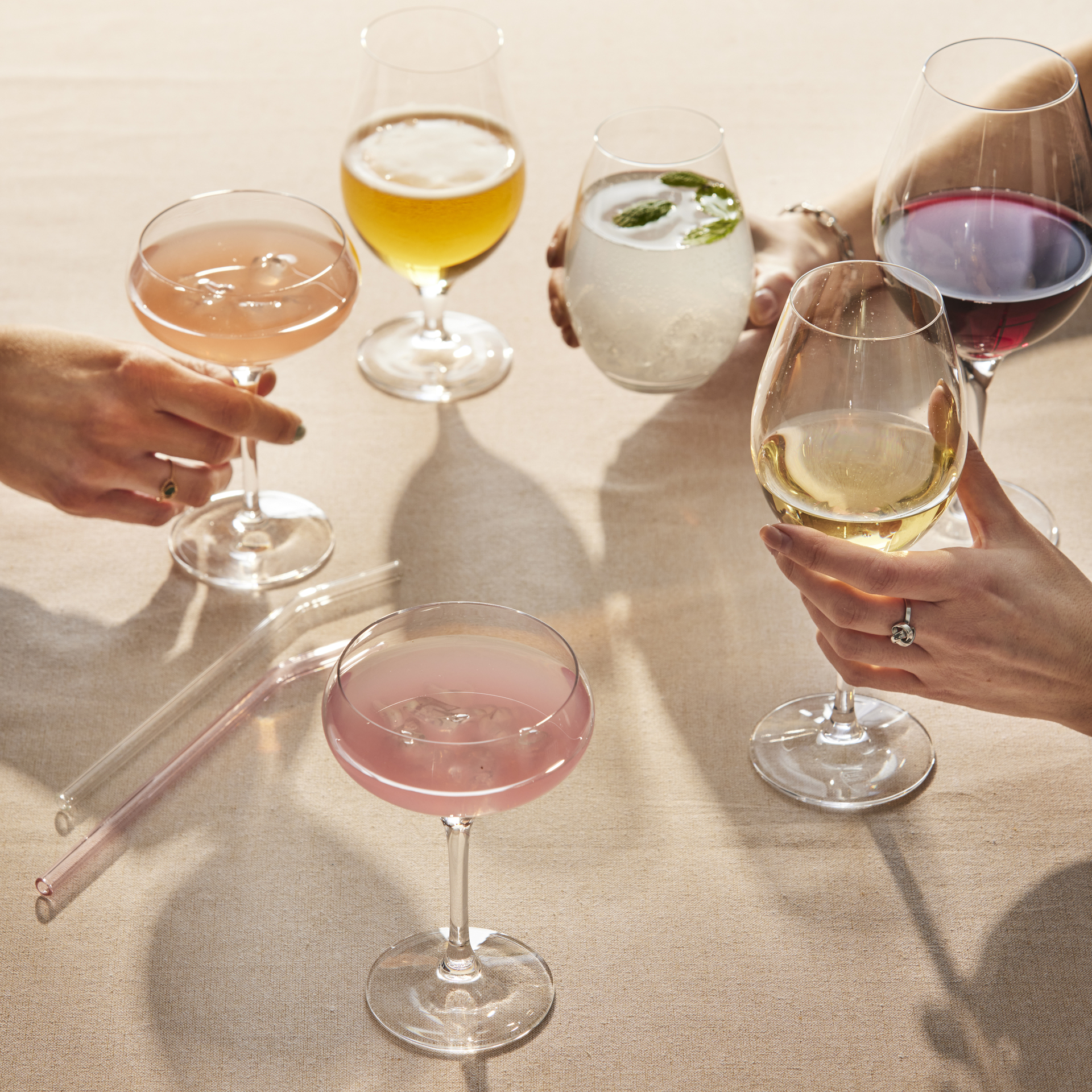 Flera händer stäcker sig över ett bord och skålar i glas fyllda med olika sorters drinkar.