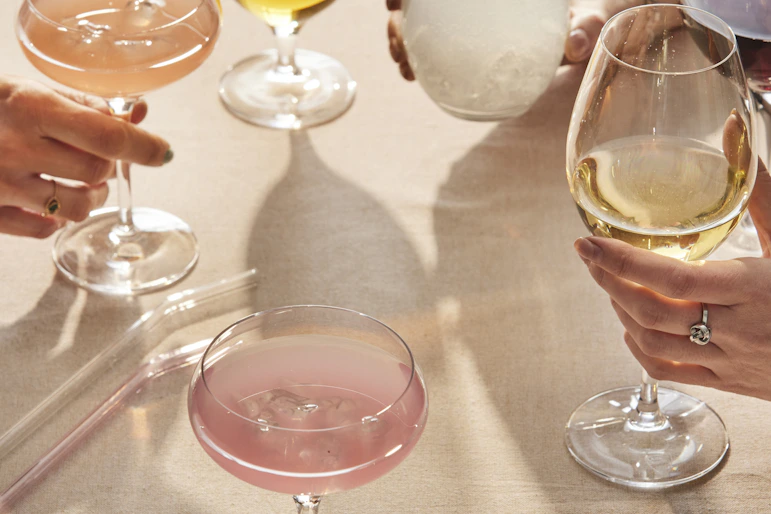 Flera händer stäcker sig över ett bord och skålar i glas fyllda med olika sorters drinkar.