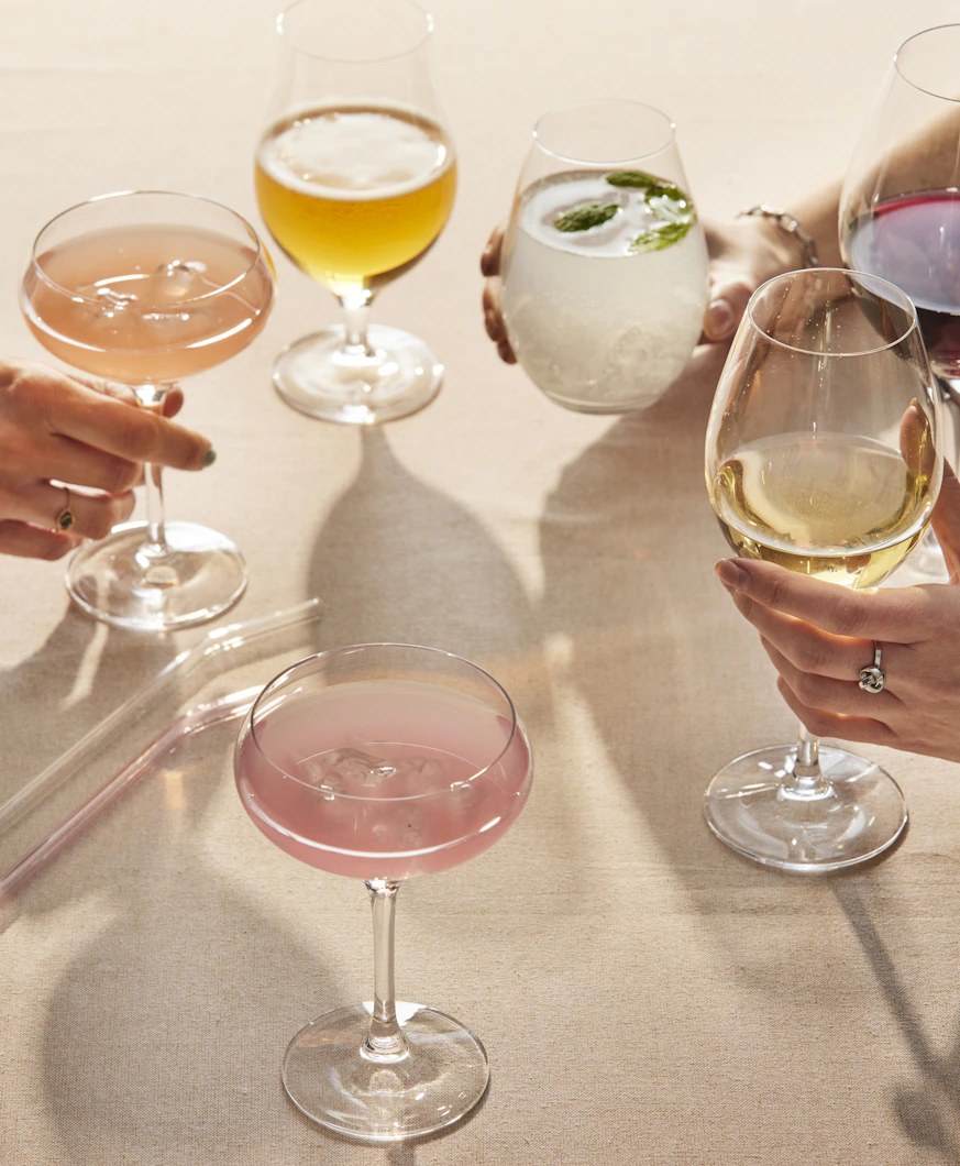 Flera händer stäcker sig över ett bord och skålar i glas fyllda med olika sorters drinkar.