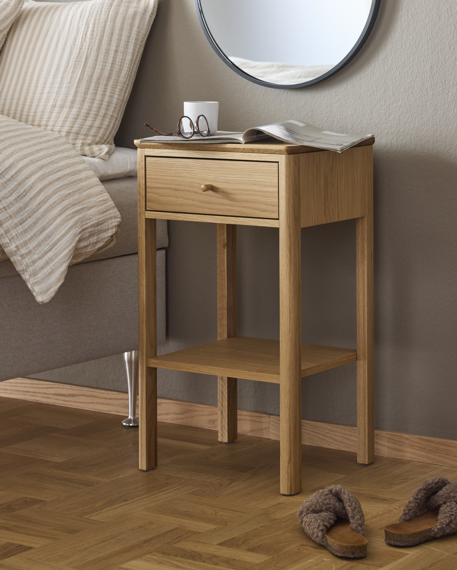 Ett sängbord i ljust trä står framför en beige vägg.