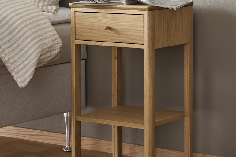 Ett sängbord i ljust trä står framför en beige vägg.