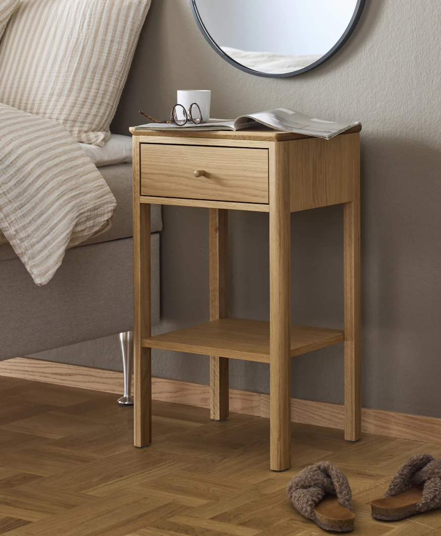 Ett sängbord i ljust trä står framför en beige vägg.