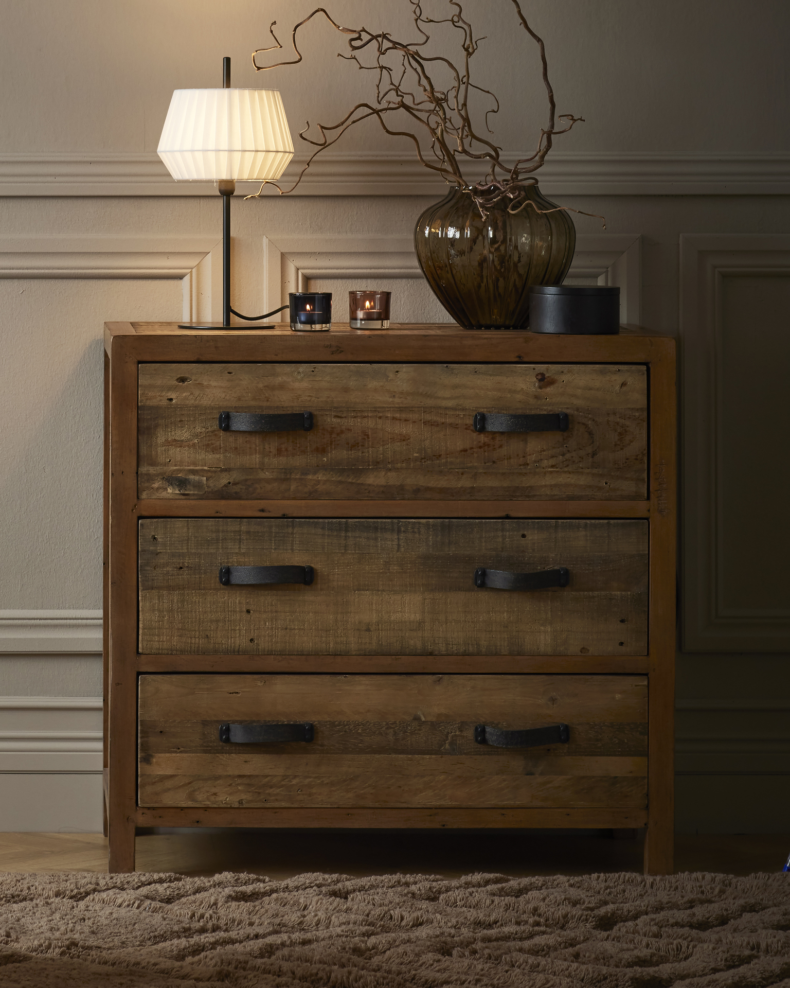 En lampa och en vas med kvistar står på en byrå i rustikt trä.