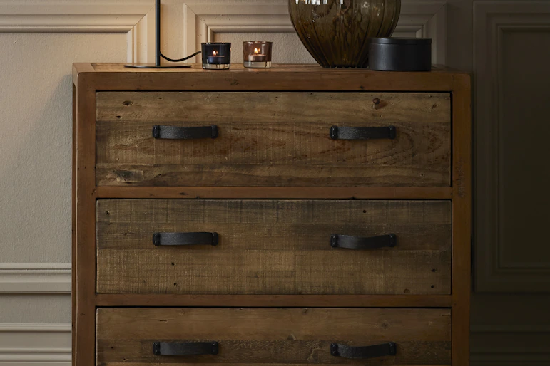 En lampa och en vas med kvistar står på en byrå i rustikt trä.