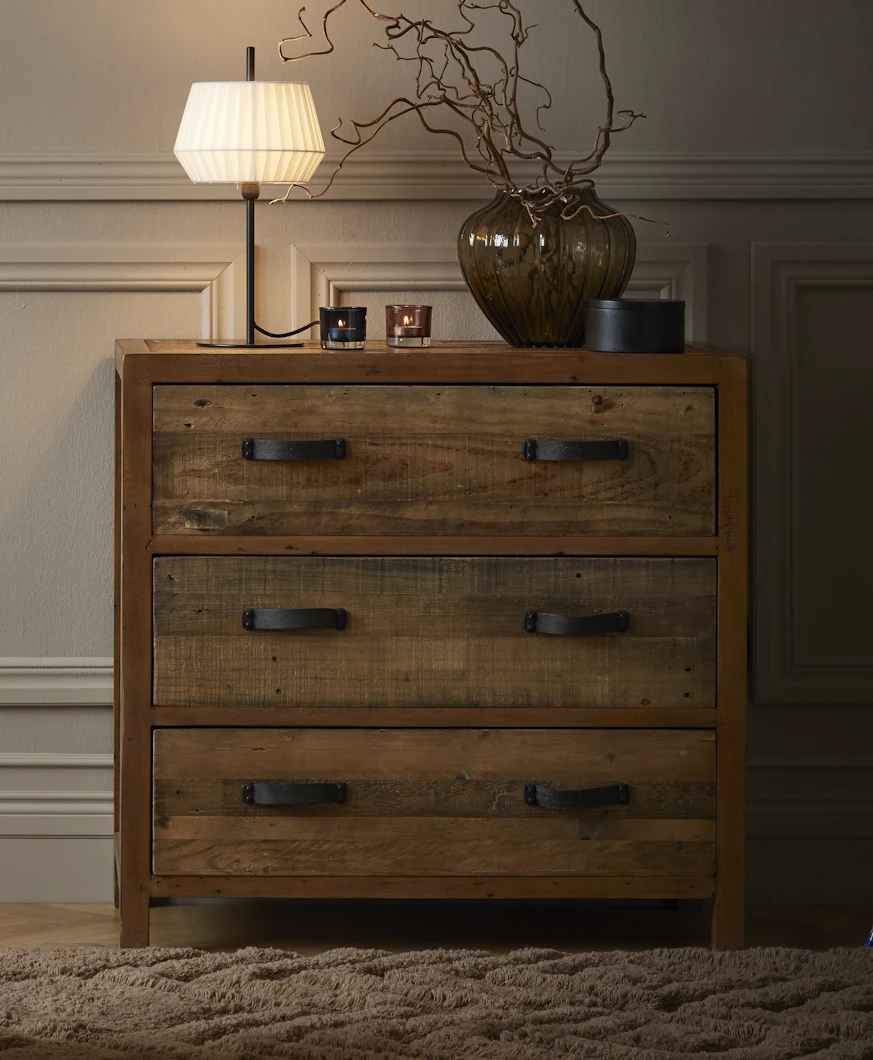 En lampa och en vas med kvistar står på en byrå i rustikt trä.