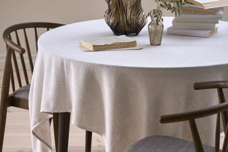 På ett runt bord finns en vit duk, en brun vas och några böcker.