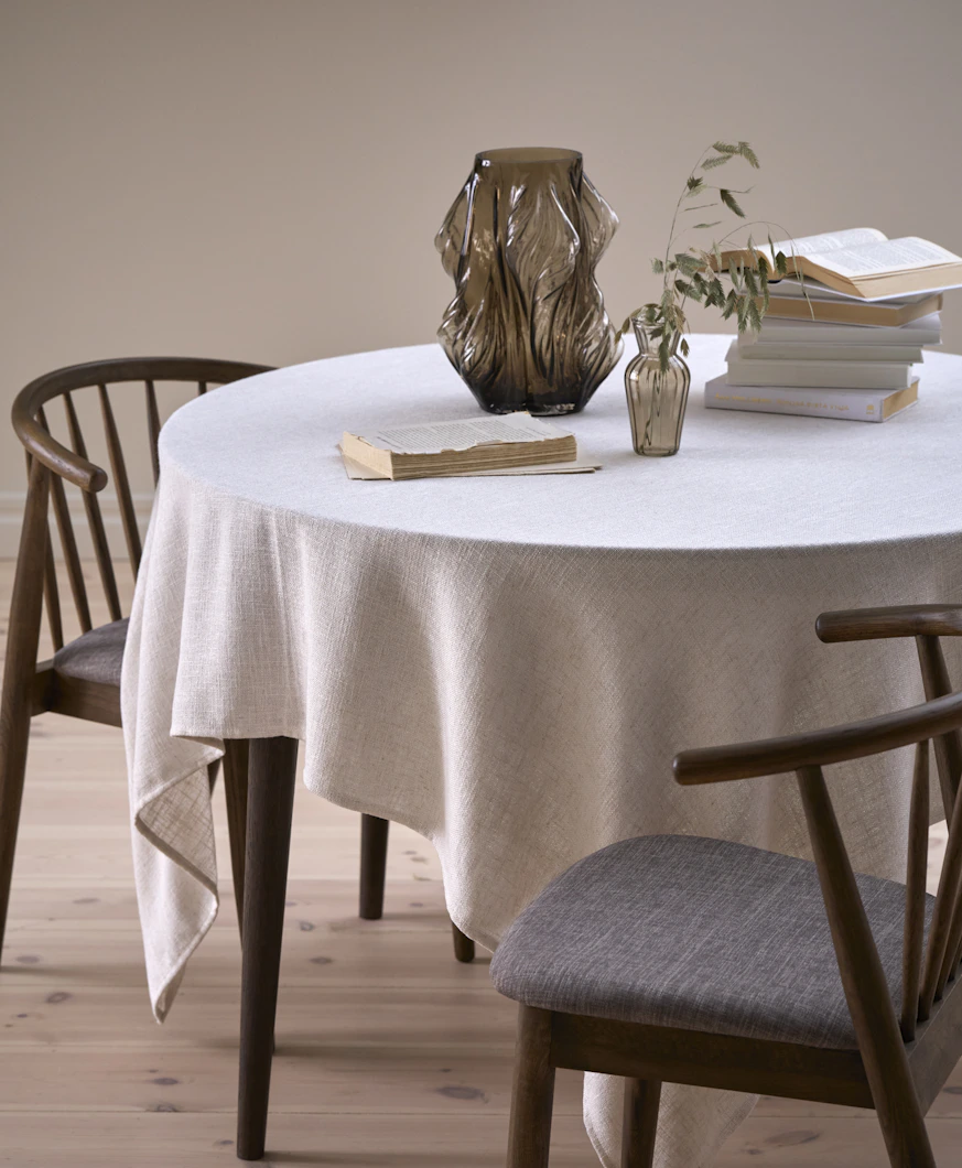 På ett runt bord finns en vit duk, en brun vas och några böcker.