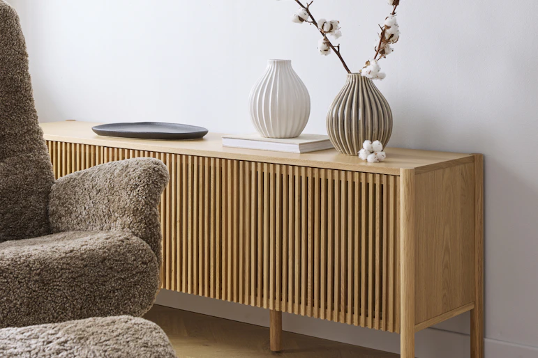 En tv-bänk med ribbad front i ljust trä står framför en vit vägg.